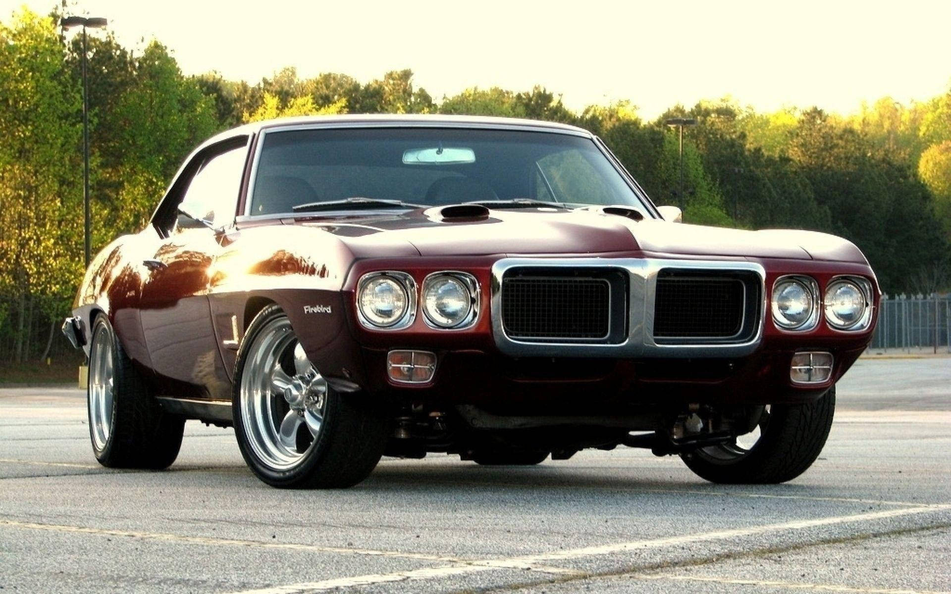 Pontiac 桌布 壁紙 — 一輛光澤的栗色經典肌肉車，帶有鍍鉻裝飾和四頭燈，停在瀝青路面上，沐浴在黃金時段的光線中。