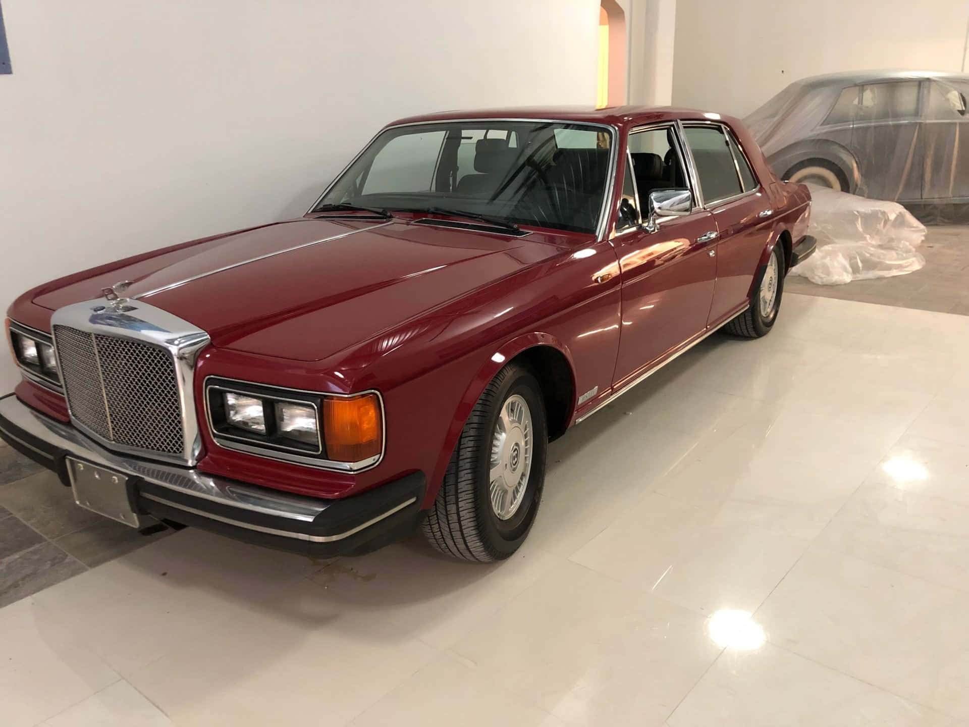 Bentley Eight 桌布 壁紙 — 一輛光澤的栗色賓利T系列轎車在明亮的燈光下，在純白色瓷磚展示間中閃閃發光。