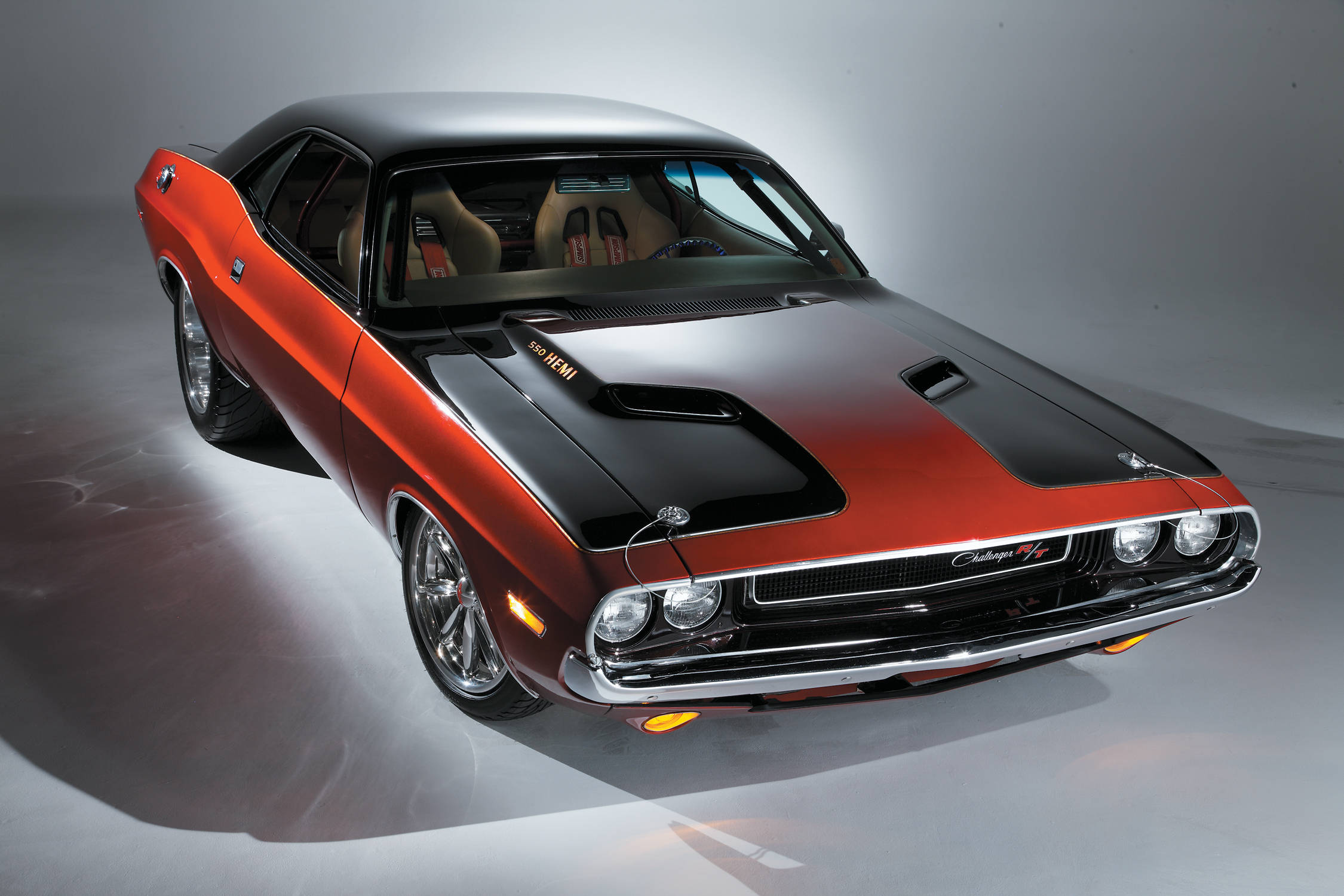 dodge iPhone 桌布 壁紙 — 一輛光澤的橙色和黑色經典肌肉車，帶有引擎蓋進氣口和鍍鉻細節，在攝影棚中以戲劇性的燈光拍攝。