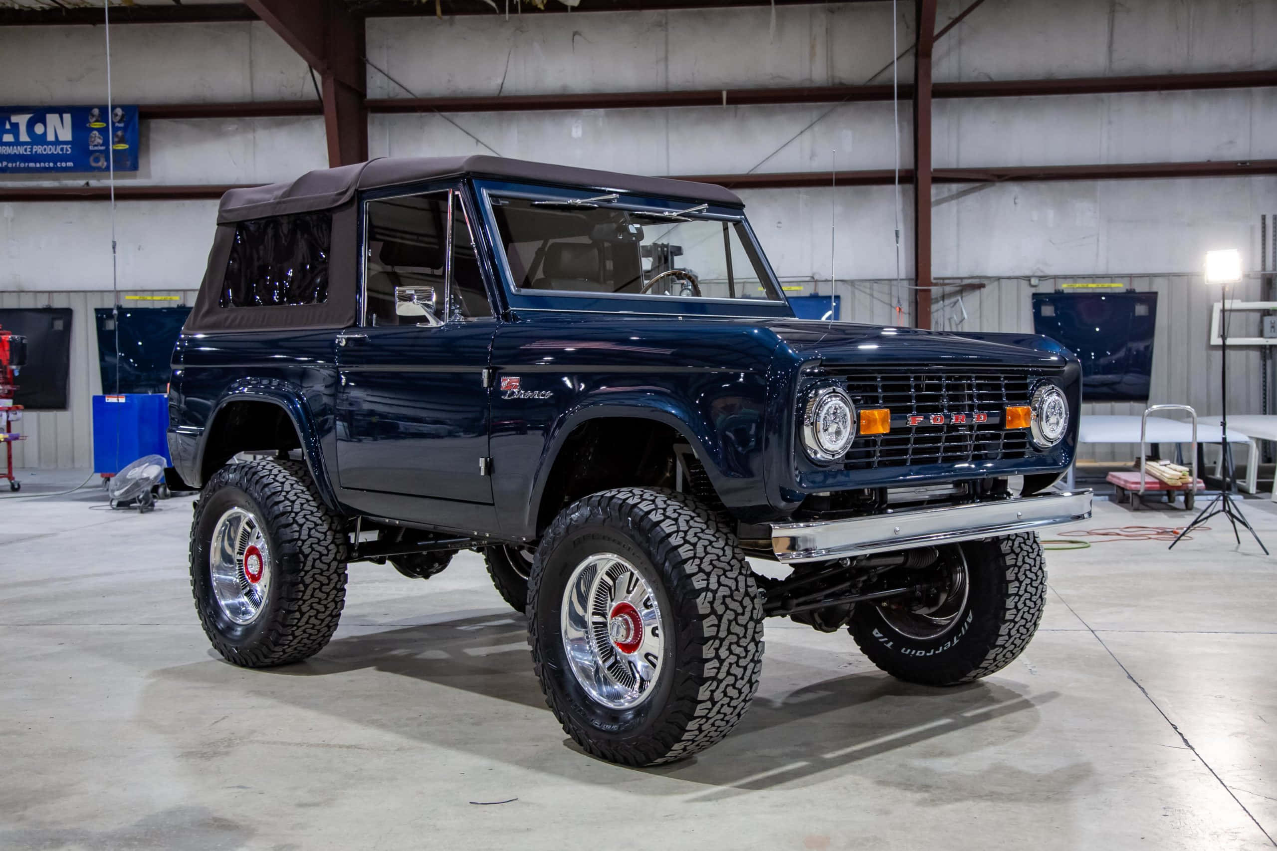 Ford Bronco 桌布 壁紙 — 一輛光澤的海軍藍色經典福特Bronco，配備超大輪胎和鍍鉻輪圈，自豪地停放在光線充足的車庫工場中。