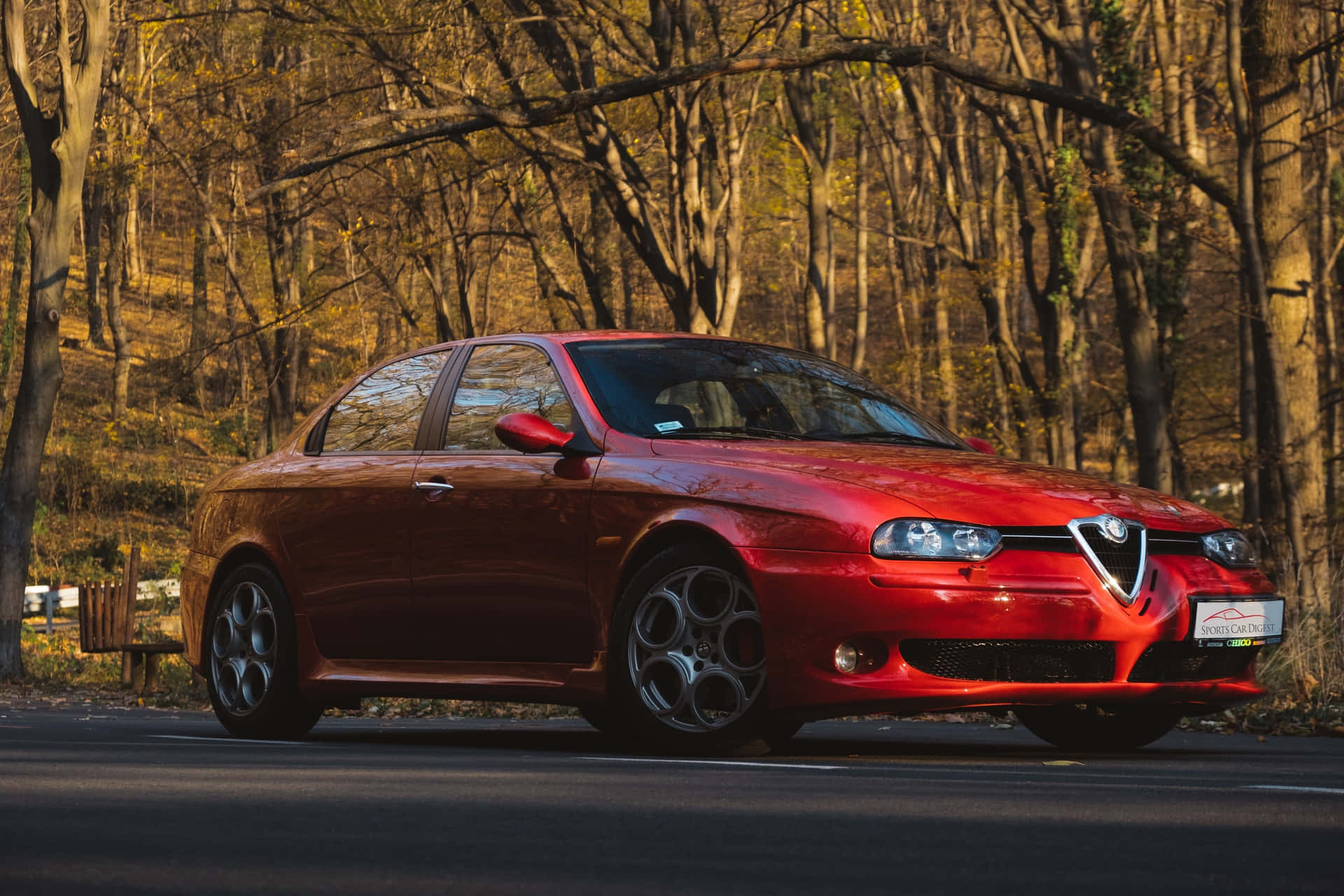Alfa Romeo 156 桌布 壁紙 — 一輛光澤的紅色 Alfa Romeo 跑車停泊在森林道路上，沐浴在金色的秋光中。