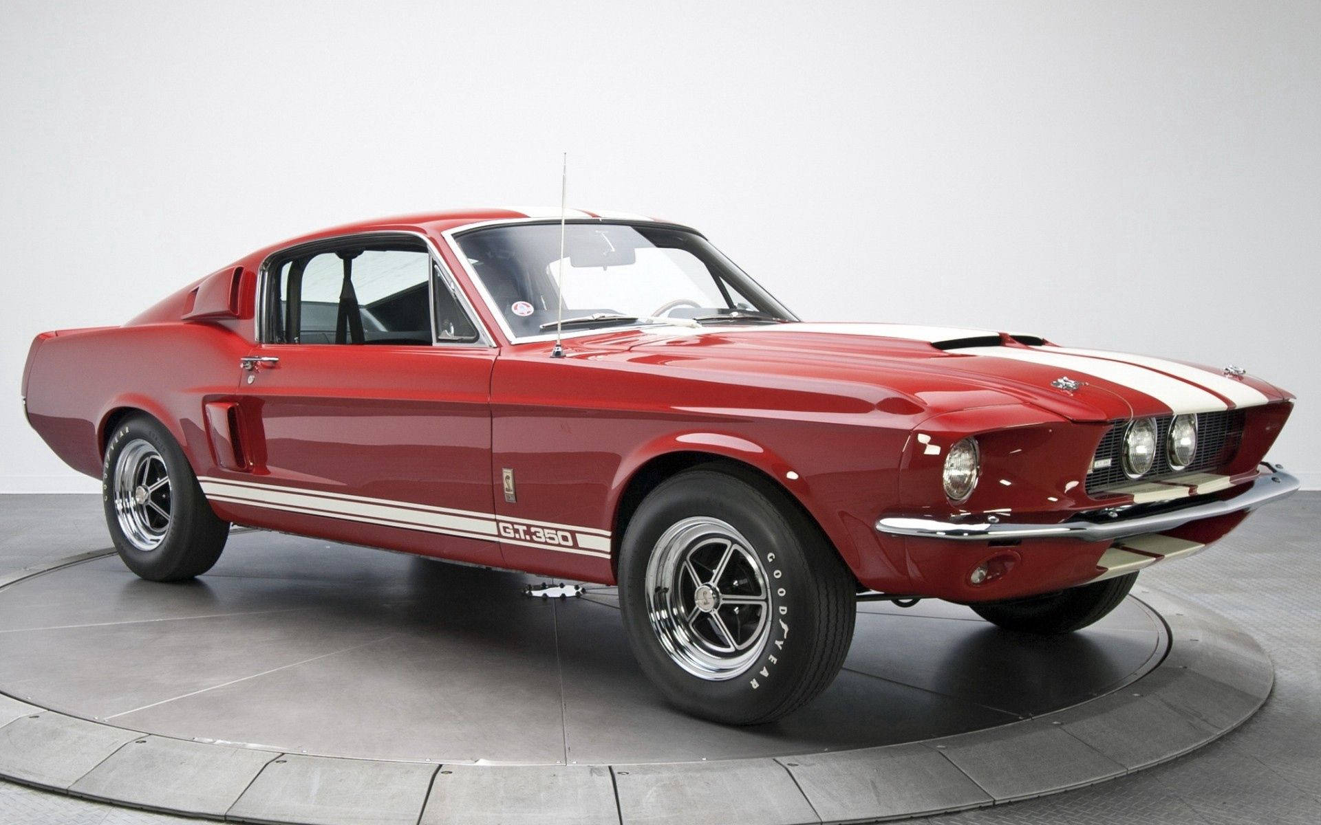 福特 桌布 壁紙 — 一輛光澤的紅色1967年Shelby GT350 Mustang，帶有白色賽車條紋，放置在白色工作室背景的圓形轉盤上。