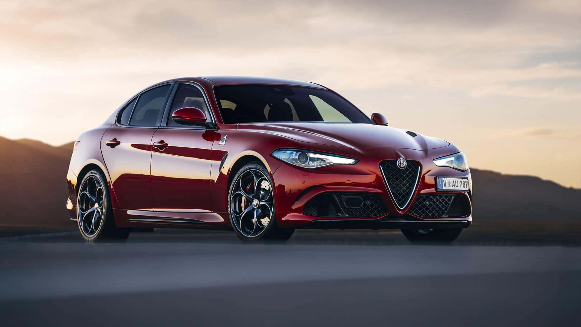 Alfa Romeo Giulia 桌布 壁紙 — 一輛光澤的紅色Alfa Romeo轎車在金色夕陽下，在遠處有山丘的沙漠道路上閃閃發光。