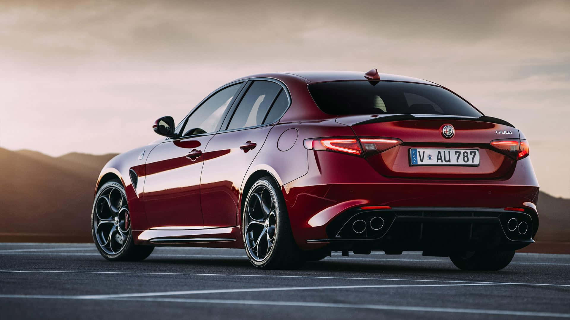 Alfa Romeo Giulia 桌布 壁紙 — 一輛光澤的紅色Alfa Romeo Giulia Quadrifoglio轎車停在瀝青路上，背景是山脈，天空柔和夕陽。