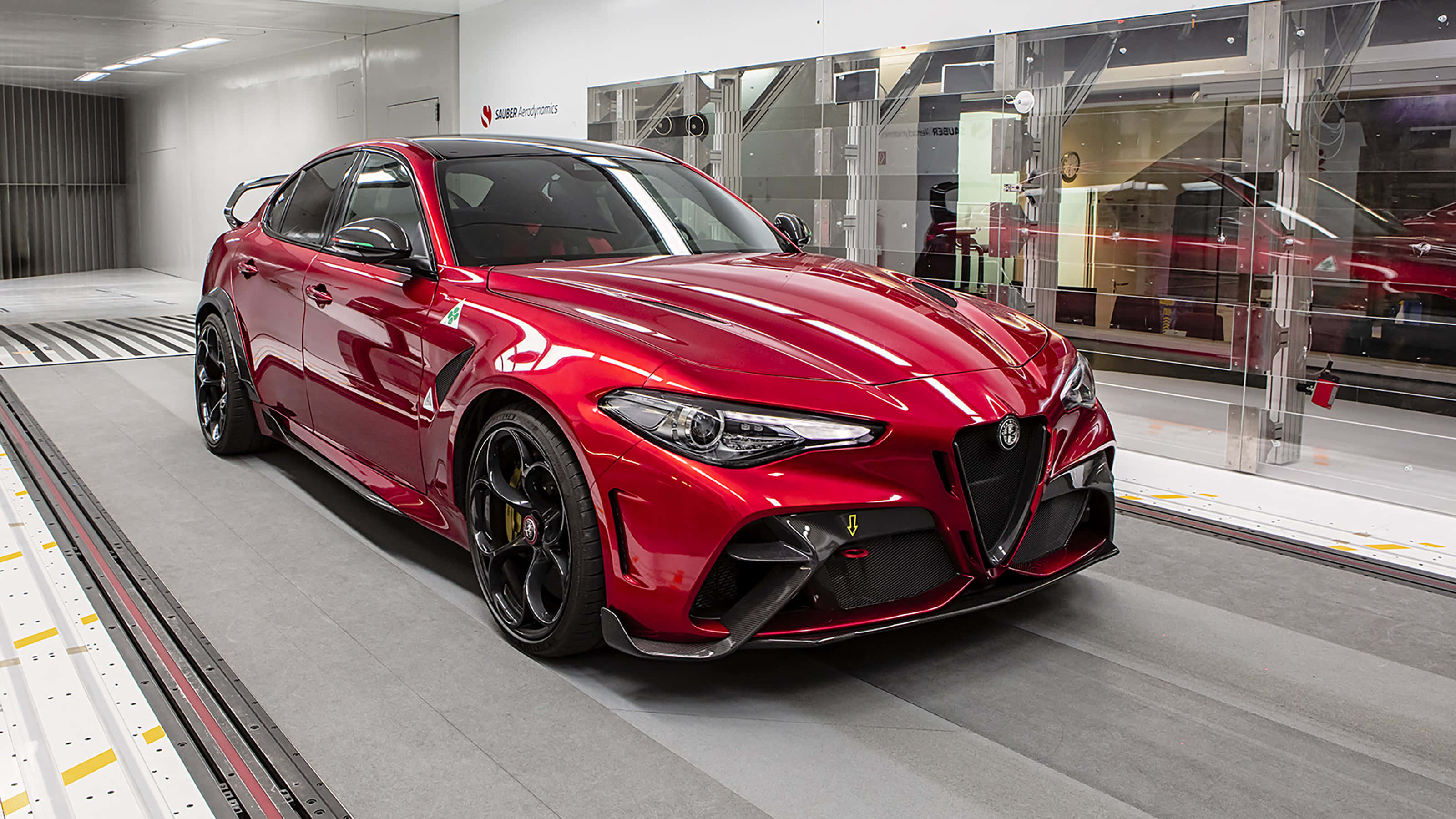 愛快羅密歐 桌布 壁紙 — 一輛光澤的紅色Alfa Romeo Giulia Quadrifoglio運動轎車在現代展廳的明亮燈光下閃耀。