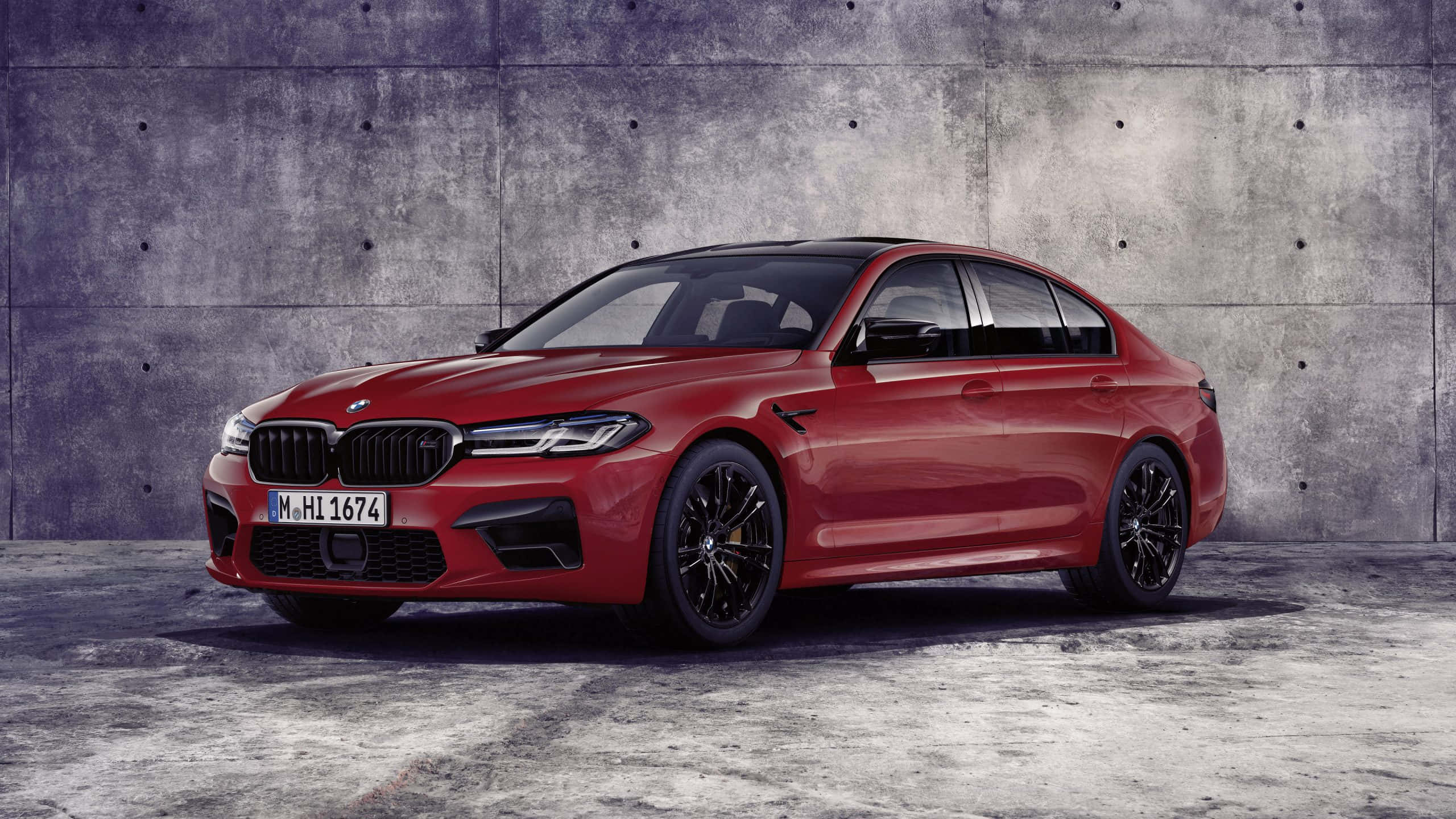 BMW 動圖 桌布 壁紙 — 一輛光澤的紅色BMW M5轎車帶有黑色飾邊，在攝影棚燈光下立於風化的混凝土牆前。