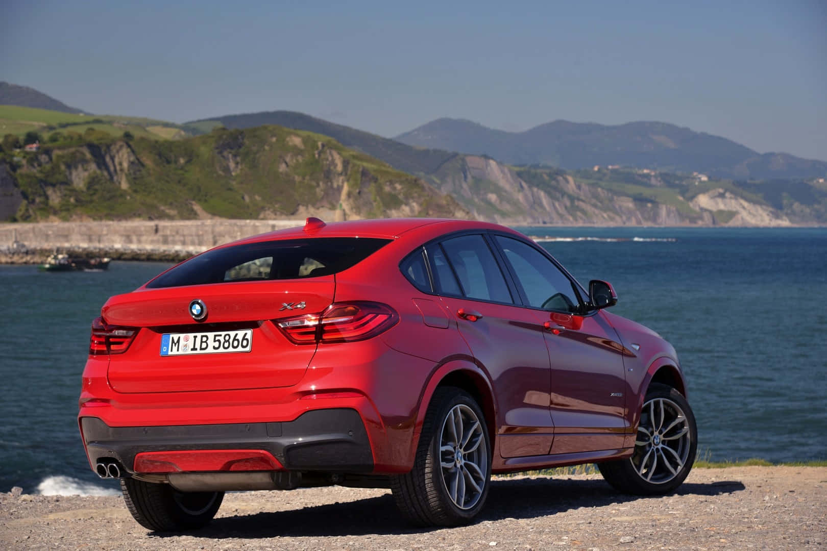 Bmw X4 桌布 壁紙 — 一輛光澤的紅色BMW X4 SUV停泊在海岸懸崖上，俯瞰深藍色的大海，背景是綠色的山丘。