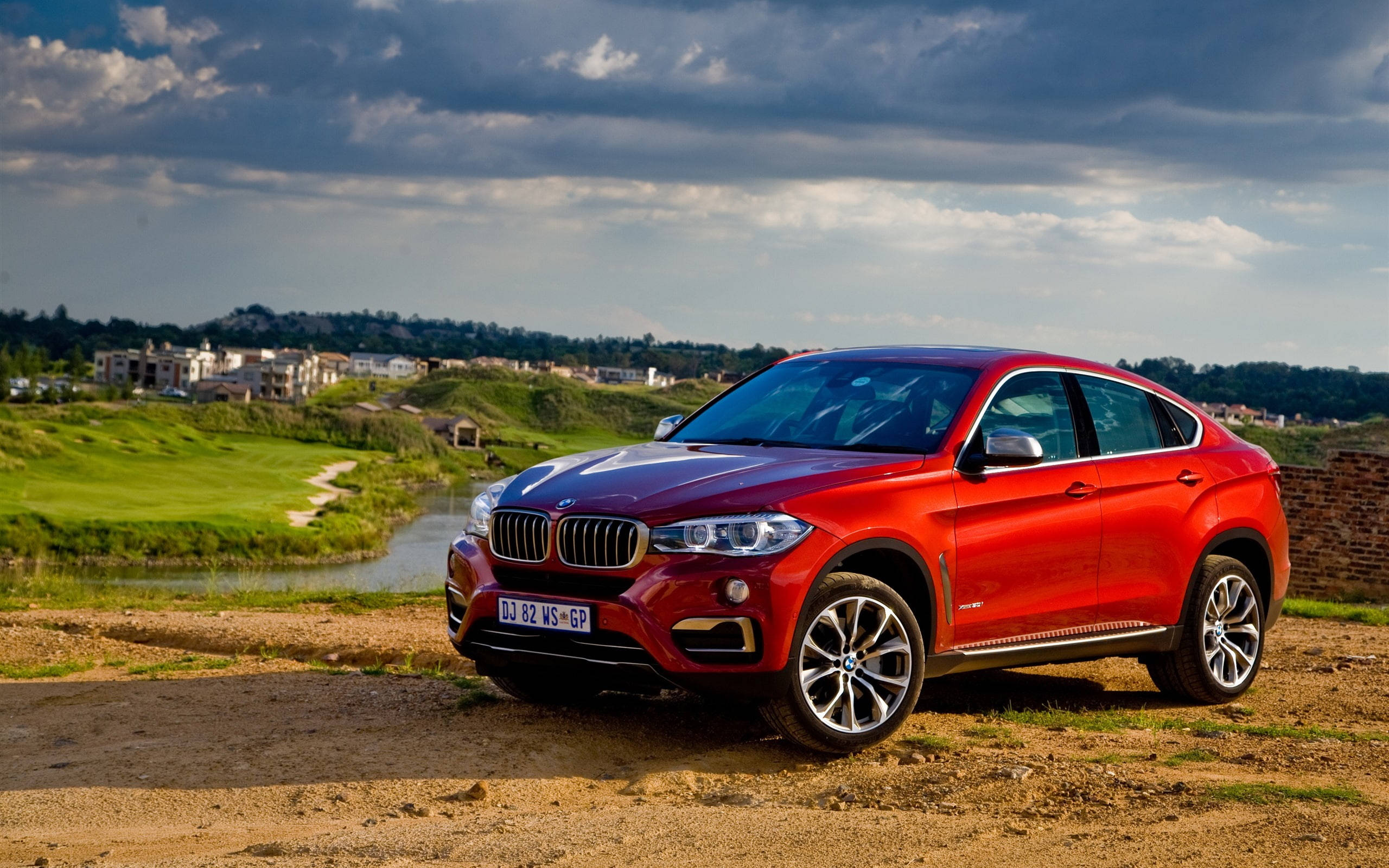 m 桌布 壁紙 — 一輛光澤的紅色BMW X6 SUV停在泥路旁的高爾夫球場邊，天空多雲，氣氛戲劇化。