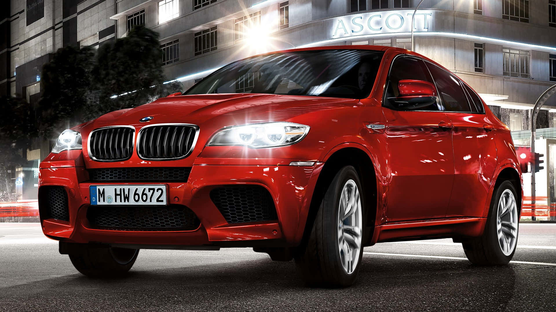 BMW X6 M 桌布 壁紙 — 一輛光澤的紅色BMW X6運動型多功能車停在夜晚潮濕的城市街道上，周圍有燈火通明的建築物和發光的車頭燈。