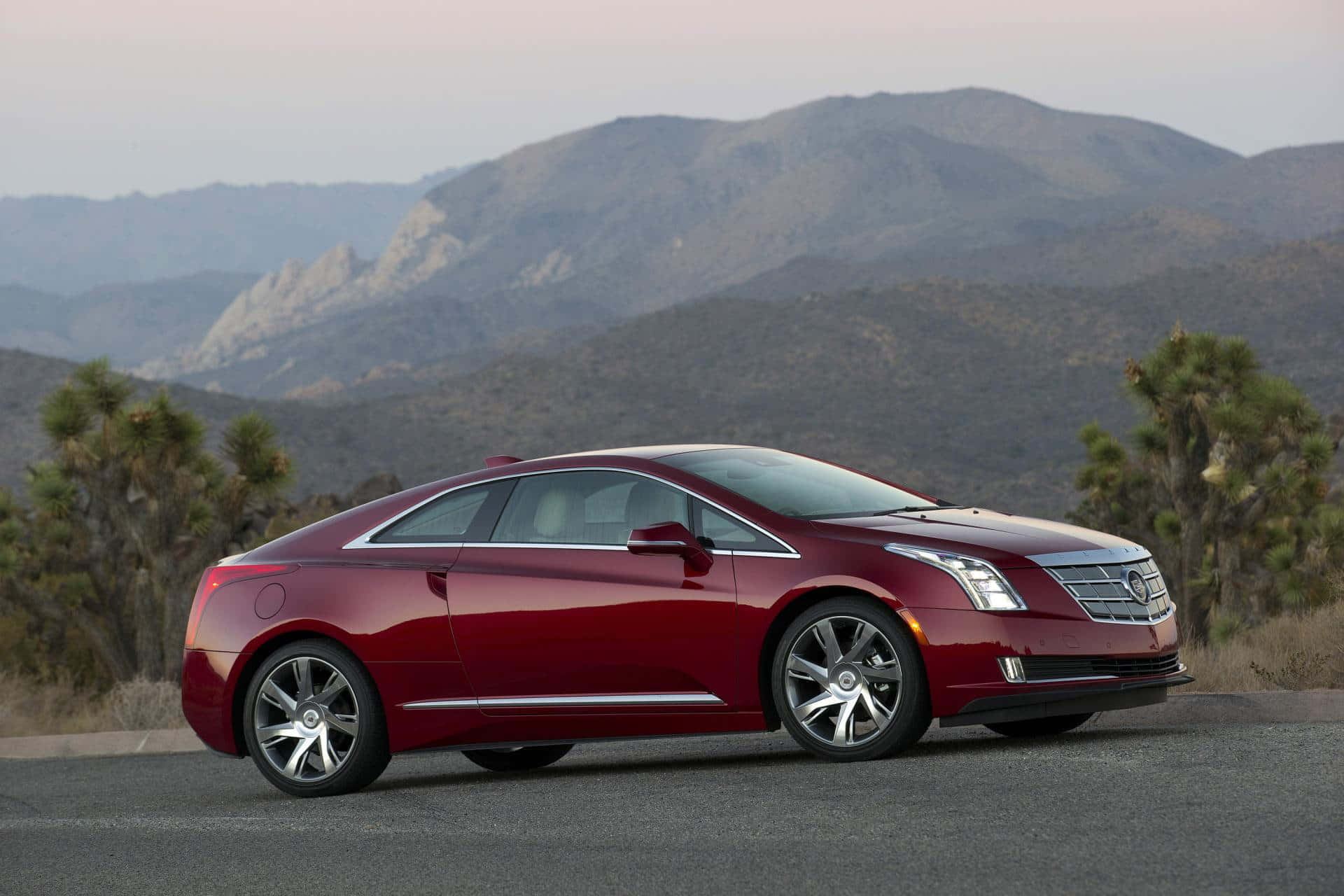 Cadillac Elr 桌布 壁紙 — 一輛光澤的紅色Cadillac ELR雙門轎跑車停在鋪砌的道路上，背景是崎嶇的山脈和沙漠樹木，在黃昏時分。