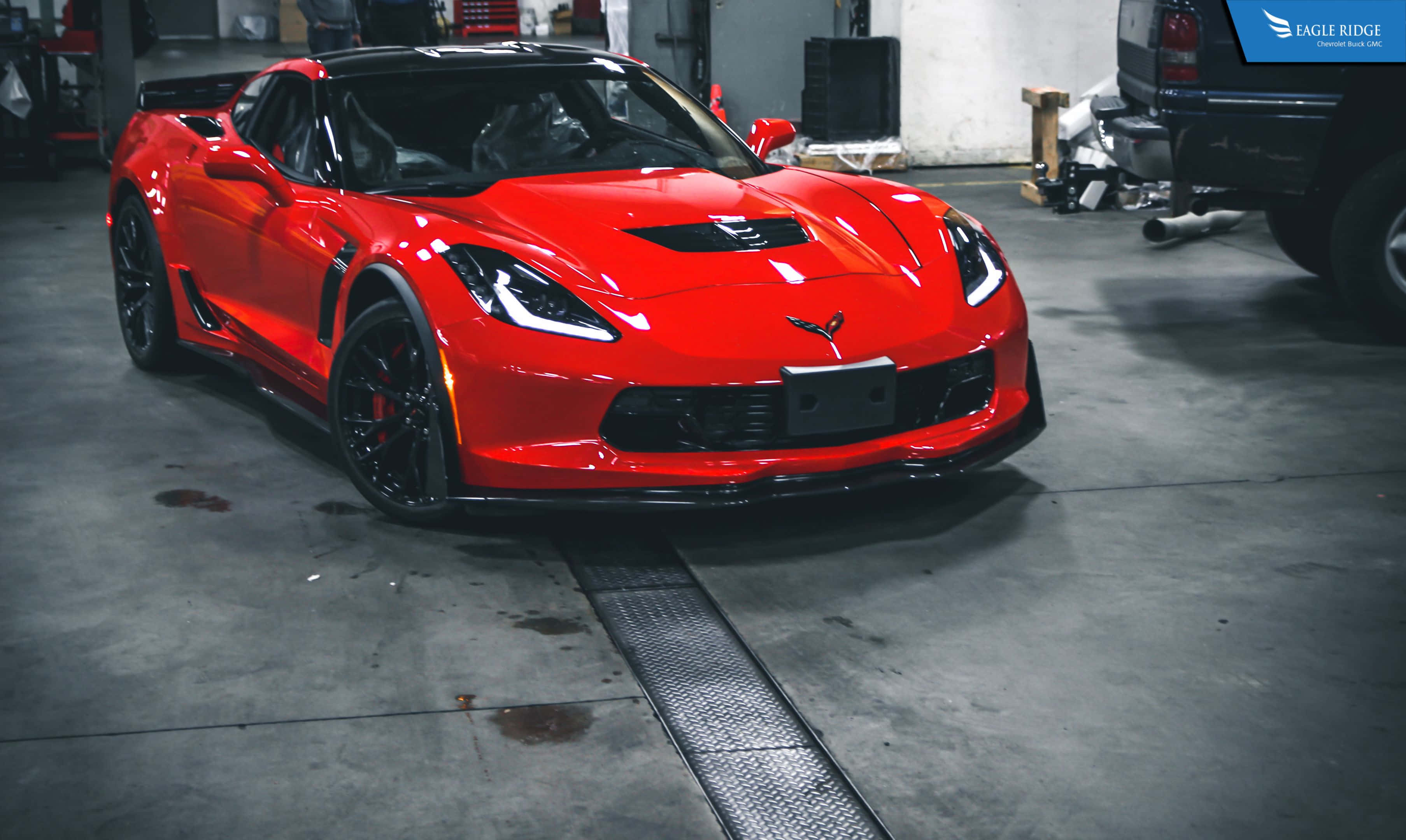 corvette 桌布 壁紙 — 一輛光澤的紅色Corvette跑車停放在光線昏暗的車庫中，背景有混凝土地板和工具。