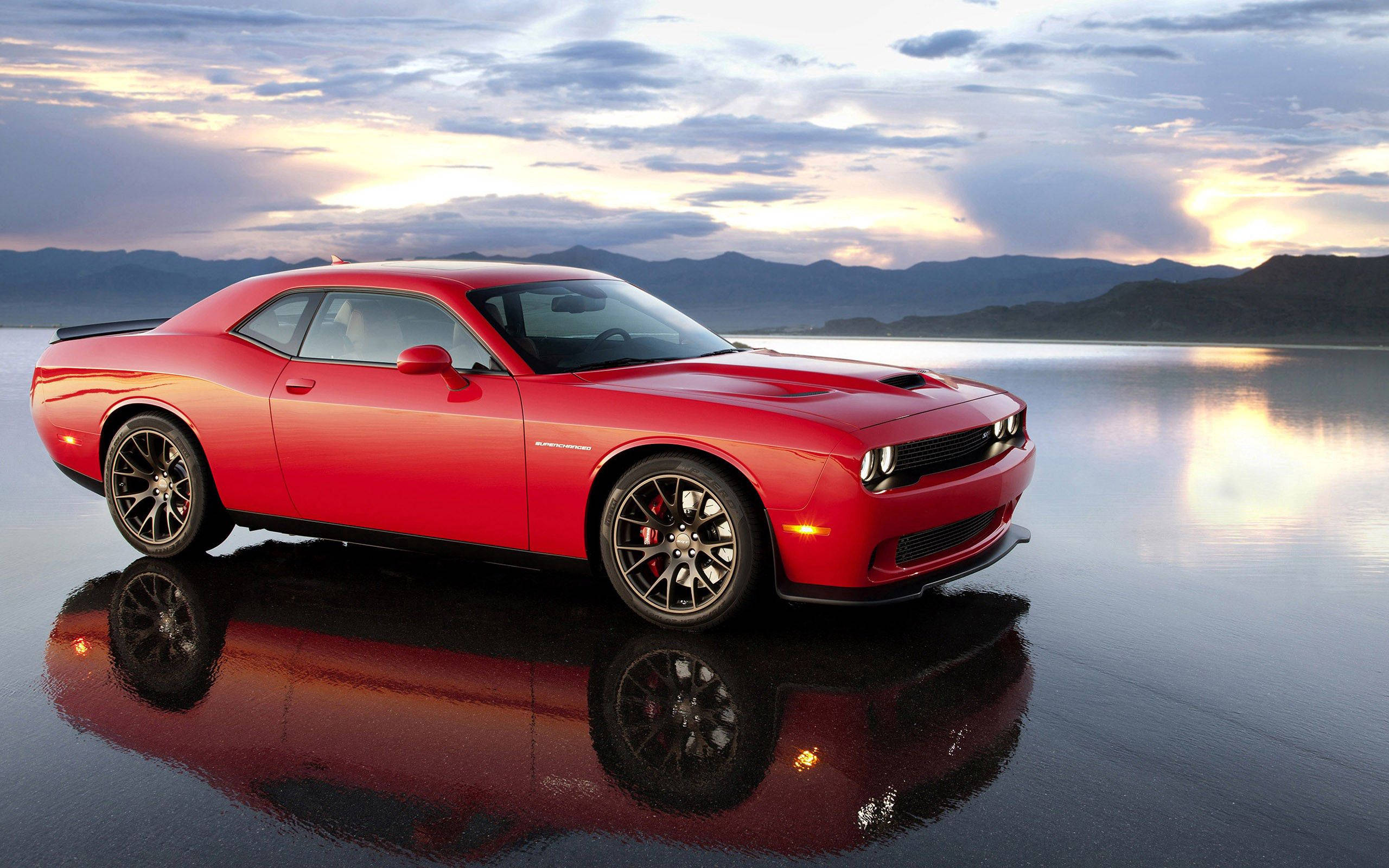 道奇隊 桌布 壁紙 — 一輛光澤的紅色Dodge Challenger在日落時分反射在濕漉漉的瀝青路面上，背景有山脈。