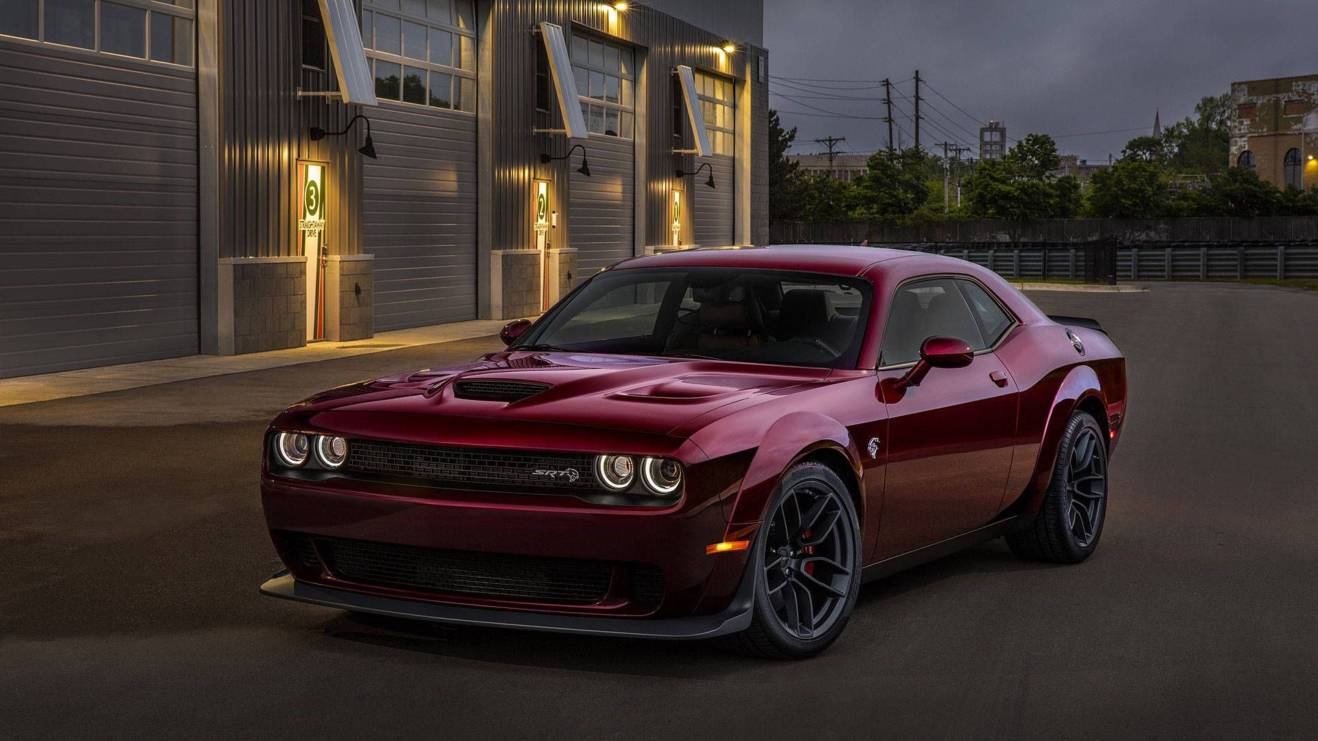 Challenger 桌布 壁紙 — 一輛光澤的紅色Dodge Challenger SRT Hellcat在黃昏時停在一座現代工業建築前。