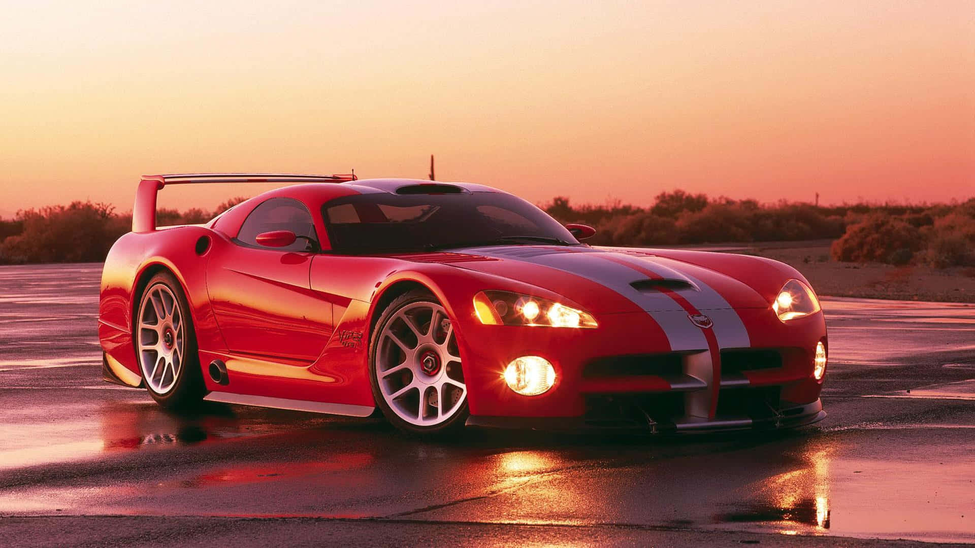 Dodge 桌布 壁紙 — 一輛光澤的紅色Dodge Viper跑車在日落時分的濕瀝青賽道上閃耀，背景是溫暖的橙色天空和沙漠灌木。