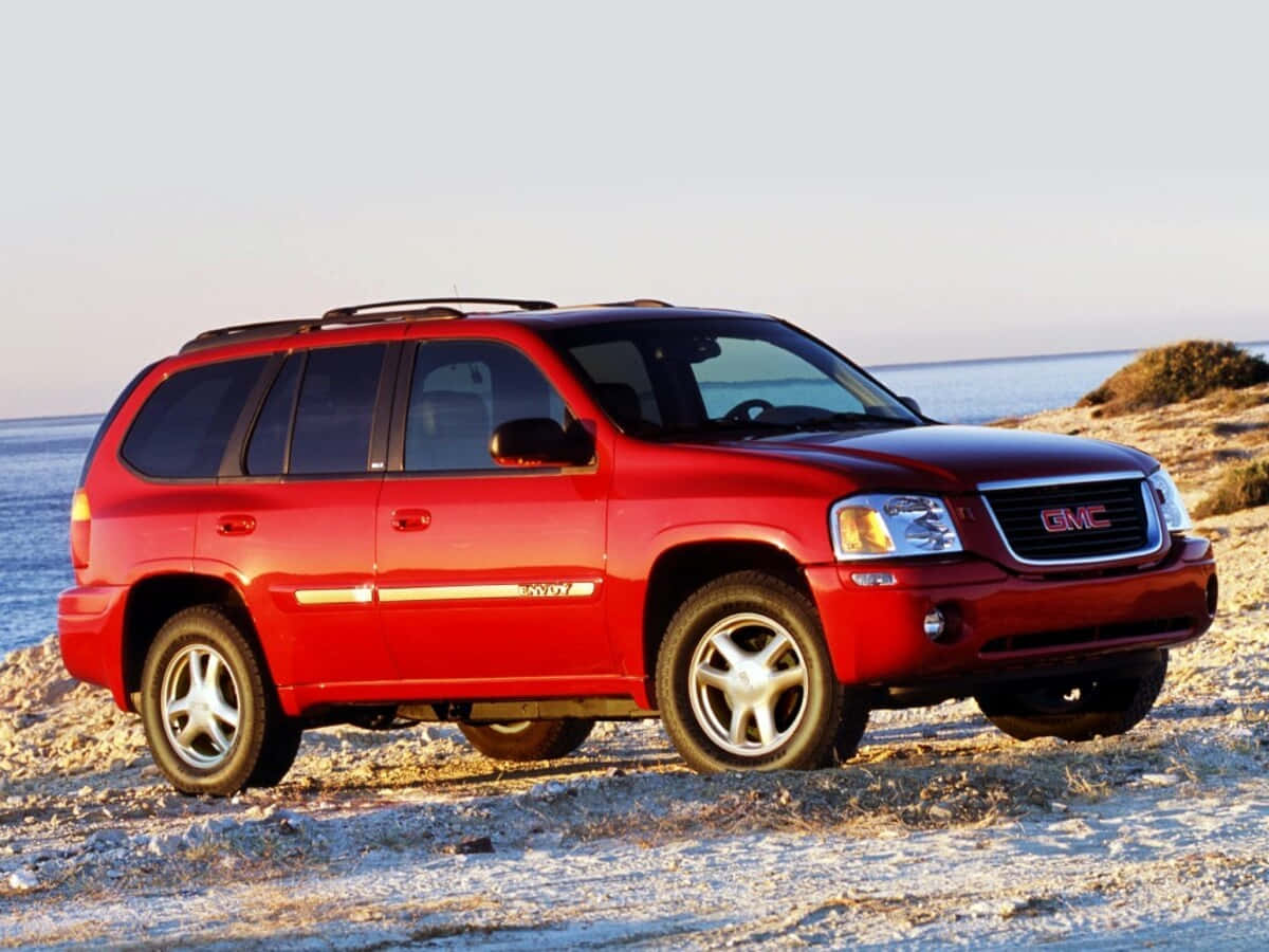 Gmc Envoy 桌布 壁紙 — 一輛光澤的紅色GMC Envoy SUV停泊在陽光明媚的海灘上，背景是海洋和天空。