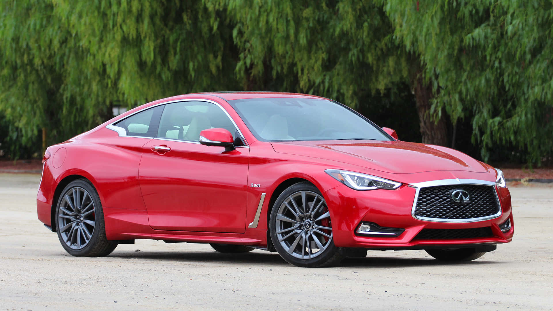 Infiniti Q60 桌布 壁紙 — 一輛光澤的紅色Infiniti Q60運動轎跑車停在碎石上，背景是茂密的綠樹。