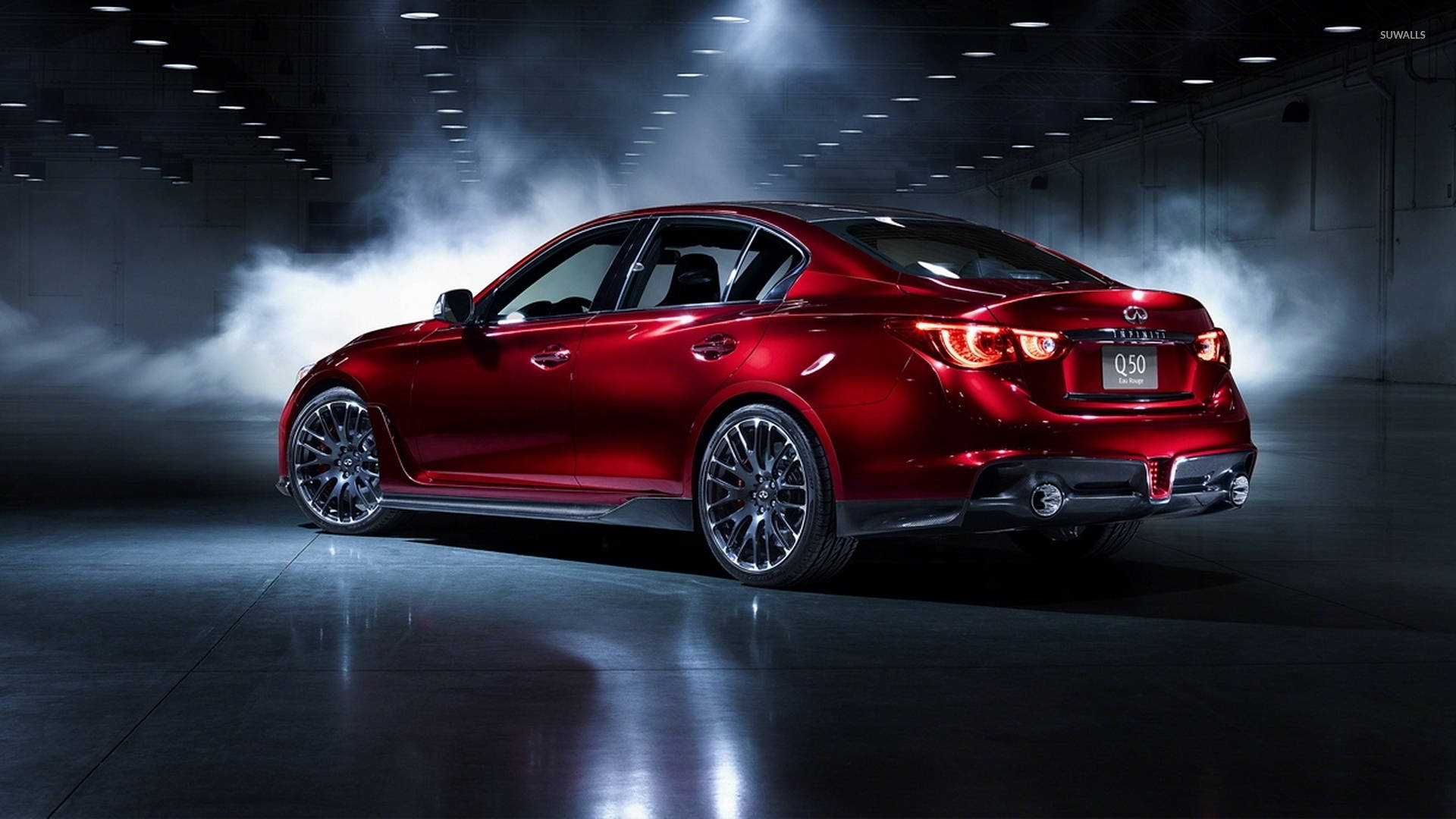 Infiniti 桌布 壁紙 — 一輛光澤的紅色Infiniti Q50轎車在黑暗的工業車庫中，於旋轉煙霧中在戲劇性的聚光燈下閃耀。