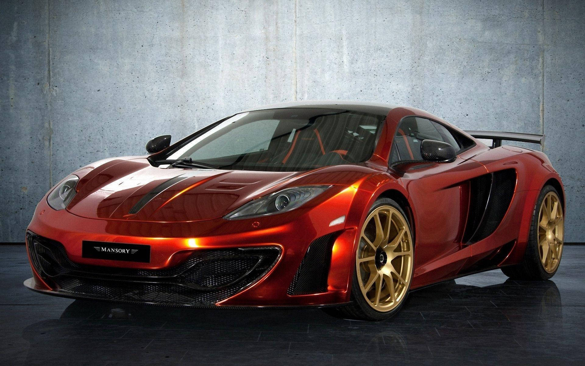 跑車 桌布 壁紙 — 一輛光澤的紅色Mansory改裝McLaren跑車，配備金色輪圈，在攝影棚燈光下對著紋理混凝土牆閃耀。