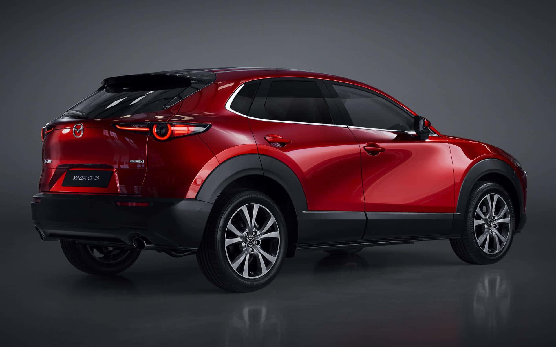 Mazda Cx-30 桌布 壁紙 — 一輛光澤的紅色Mazda CX-30 SUV在攝影棚內展示，配有戲劇性燈光和反射地板。