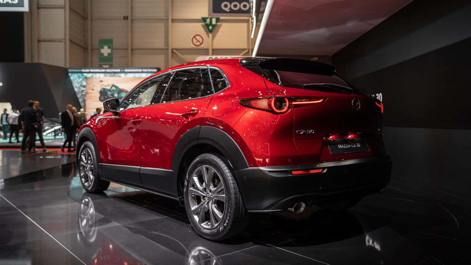 Mazda Cx-30 桌布 壁紙 — 一輛光澤的紅色Mazda CX-30 SUV在車展上展示，配有拋光黑色地板和明亮的展覽燈光。