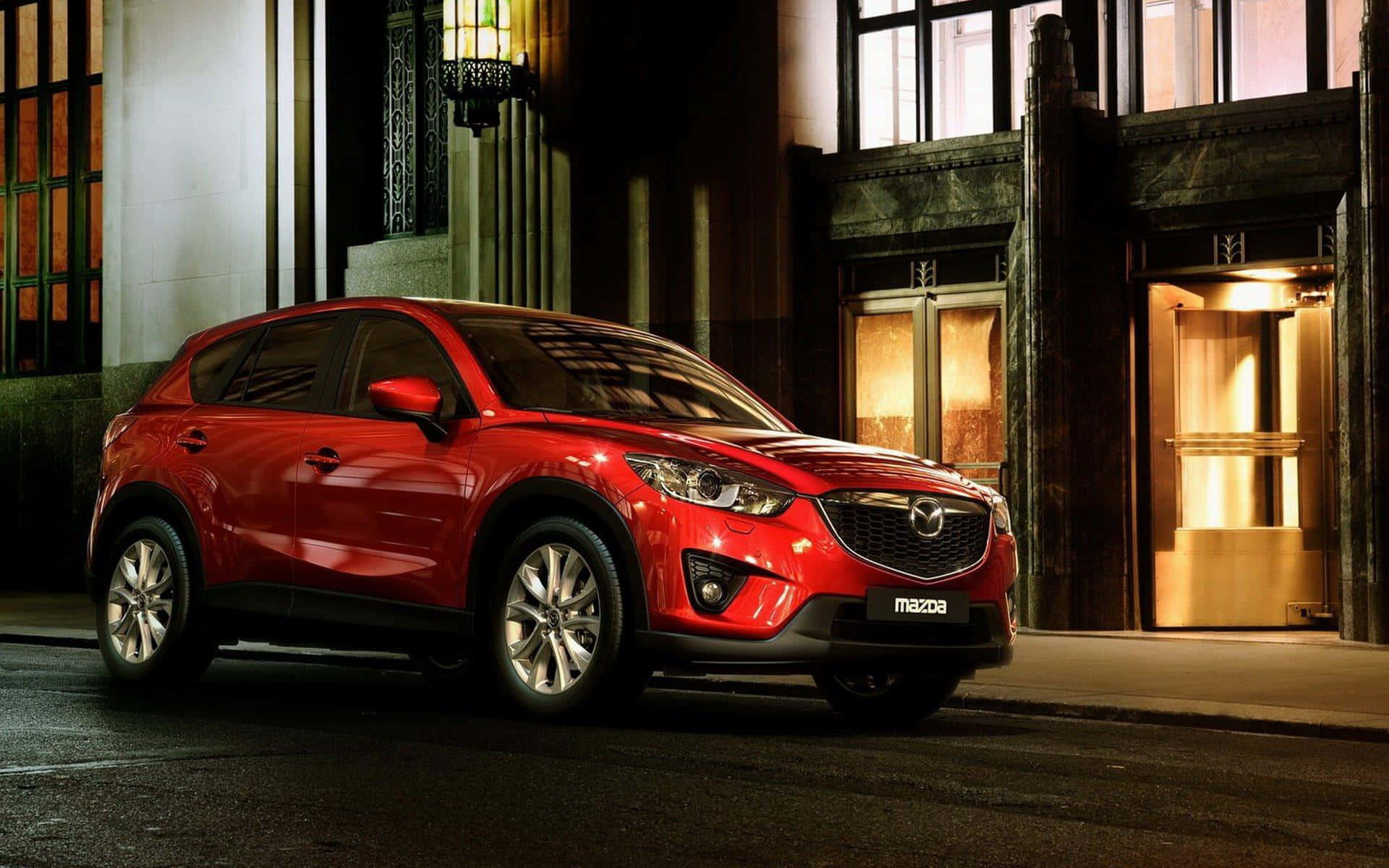 Mazda Cx-5 桌布 壁紙 — 一輛光澤的紅色Mazda CX-5 SUV在夜間停泊在一個有溫暖金色燈光的裝飾藝術風格建築前。