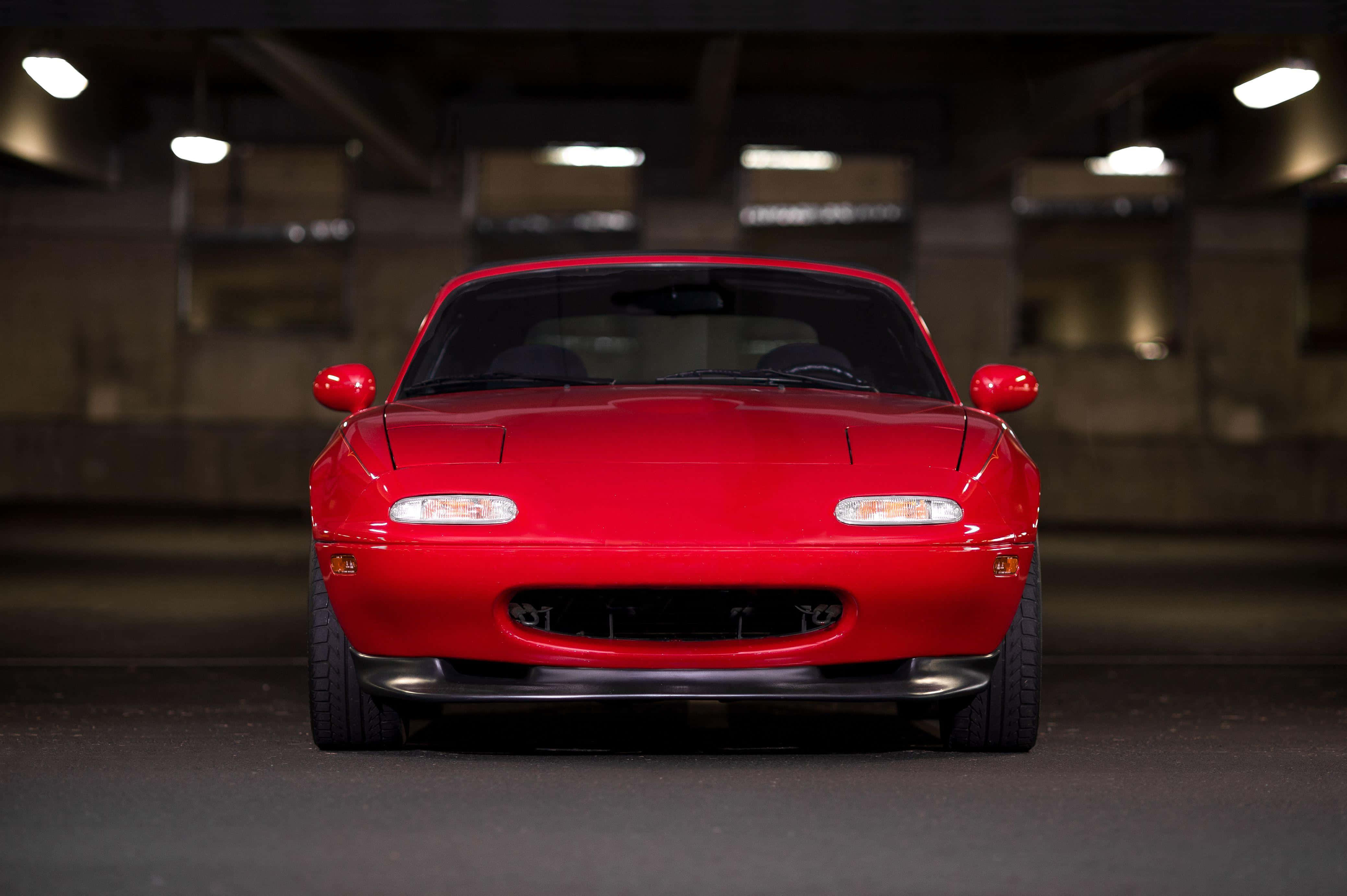 跑車 桌布 壁紙 — 一輛光澤的紅色Mazda Miata跑車在燈光昏暗的地下停車場中向前，天花板上掛著燈。
