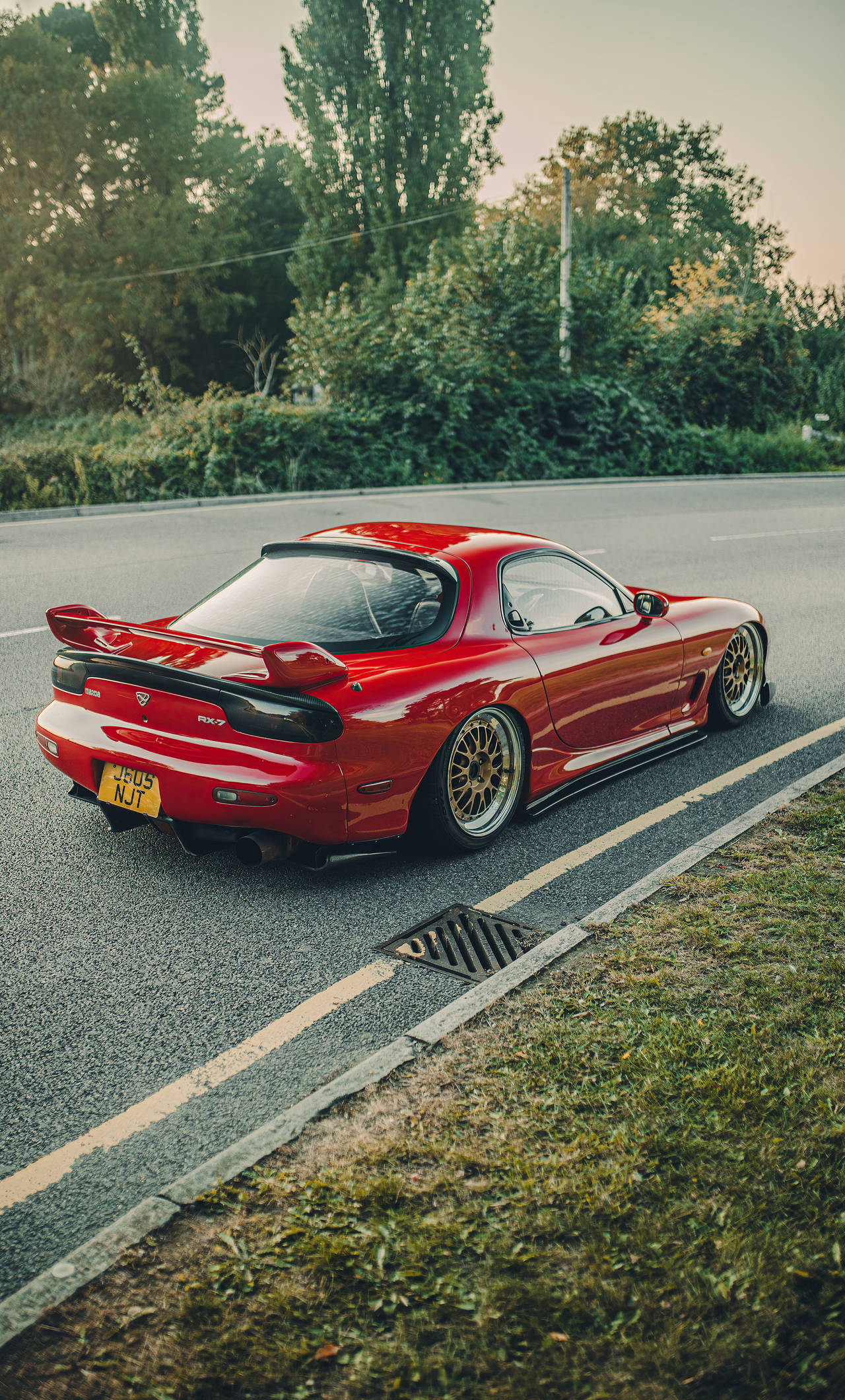 Sports Cars 桌布 壁紙 — 一輛光澤的紅色Mazda RX-7跑車配金色輪圈，在黃金時刻停泊在路邊。
