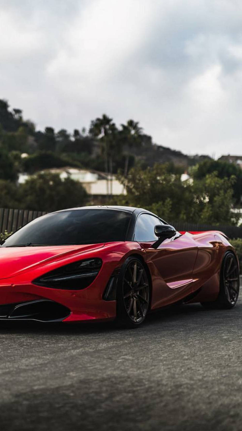 跑車 桌布 壁紙 — 一輛光澤的紅色McLaren 720S跑車停在瀝青路上，背景有棕櫚樹和山丘，天空多雲。