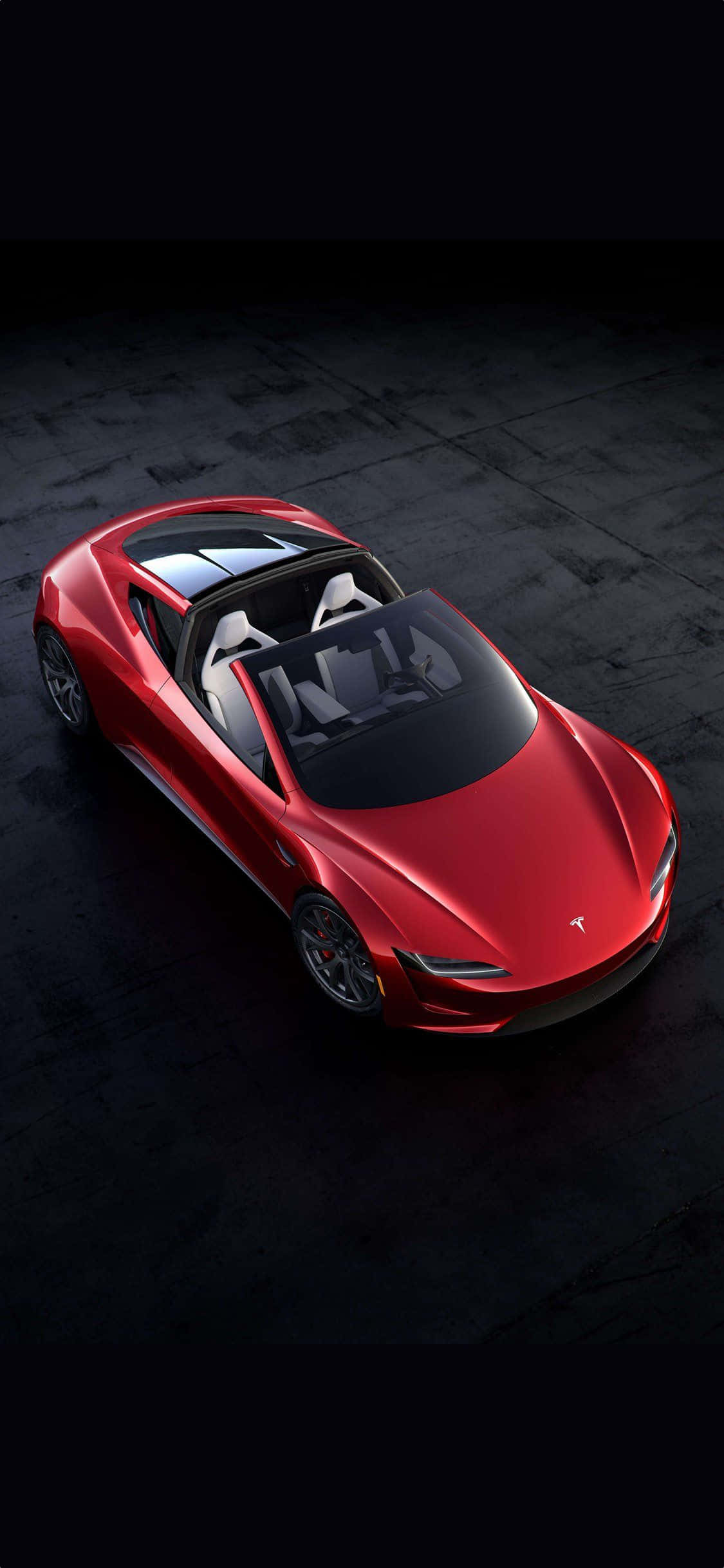 特斯拉 桌布 壁紙 — 一輛光澤的紅色Tesla Roadster敞篷車，白色座椅，置於深色混凝土地板中央，在戲劇性的工作室燈光下。