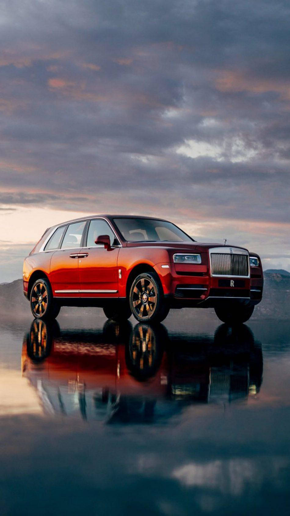 Royce 桌布 壁紙 — 一輛光澤的紅色勞斯萊斯 Cullinan SUV 在戲劇性的暮色天空下完美地反射在潮濕的路面上。