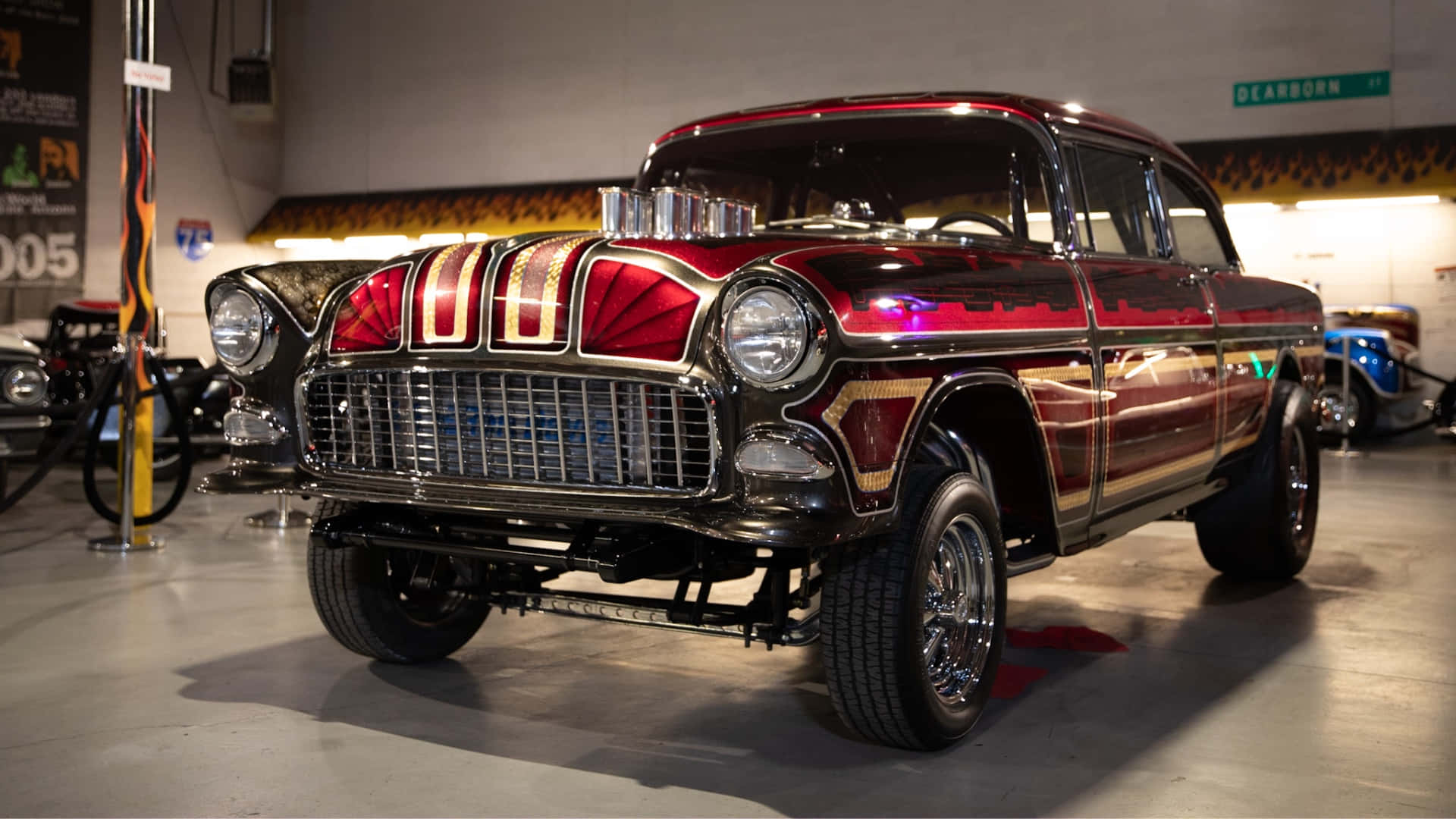 酷車 桌布 壁紙 — 一輛光澤的紅色和金色定制1950年代雪佛蘭，帶有鍍鉻細節和升高懸掛，在光線充足的室內汽車展廳中展示。