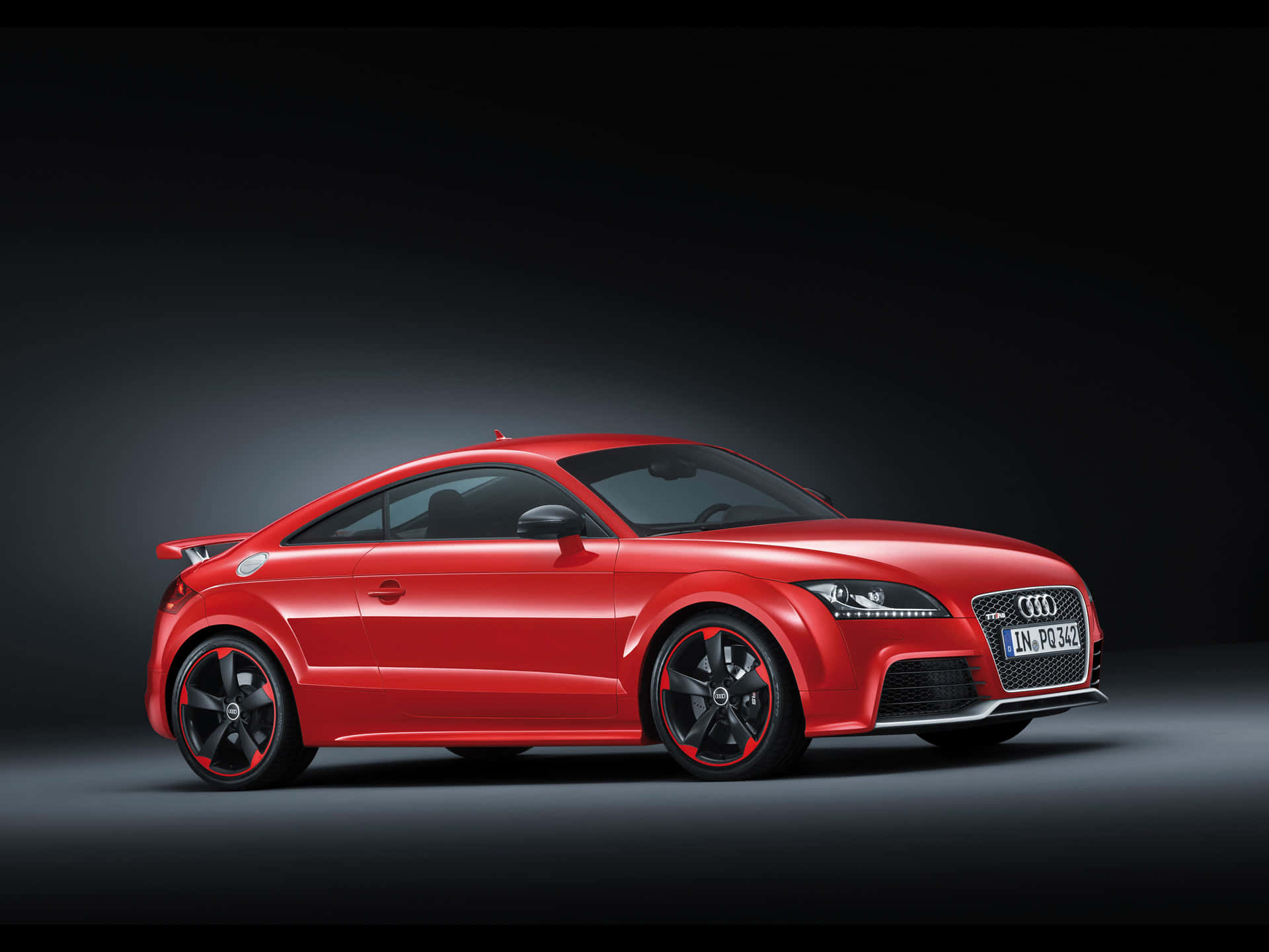 Audi Tt Rs 桌布 壁紙 — 一輛光澤的紅色奧迪TT RS跑車，帶有黑色飾邊和紅色輪圈細節，在深色工作室背景下擺拍。