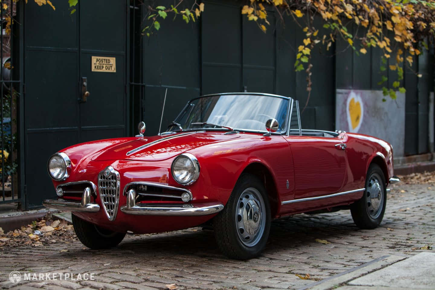 Alfa Romeo Spider 桌布 壁紙 — 一輛光澤的紅色復古愛快羅密歐Spider敞篷車停泊在鵝卵石街道上，上方有秋葉。