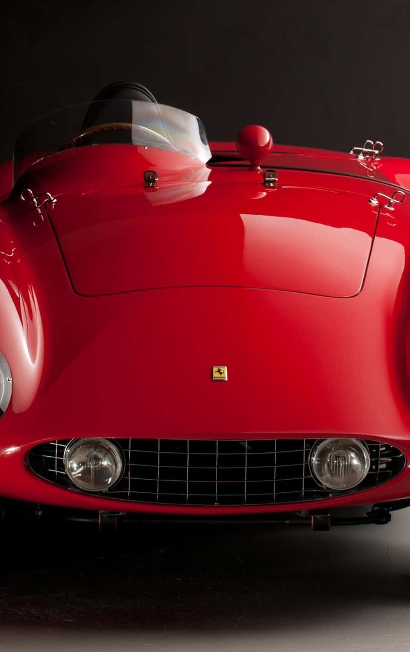 Vintage Ferrari 桌布 壁紙 — 一輛光澤的紅色復古法拉利跑車，帶有鍍鉻裝飾和圓形頭燈，在黑暗背景下的戲劇性工作室拍攝中被捕捉。