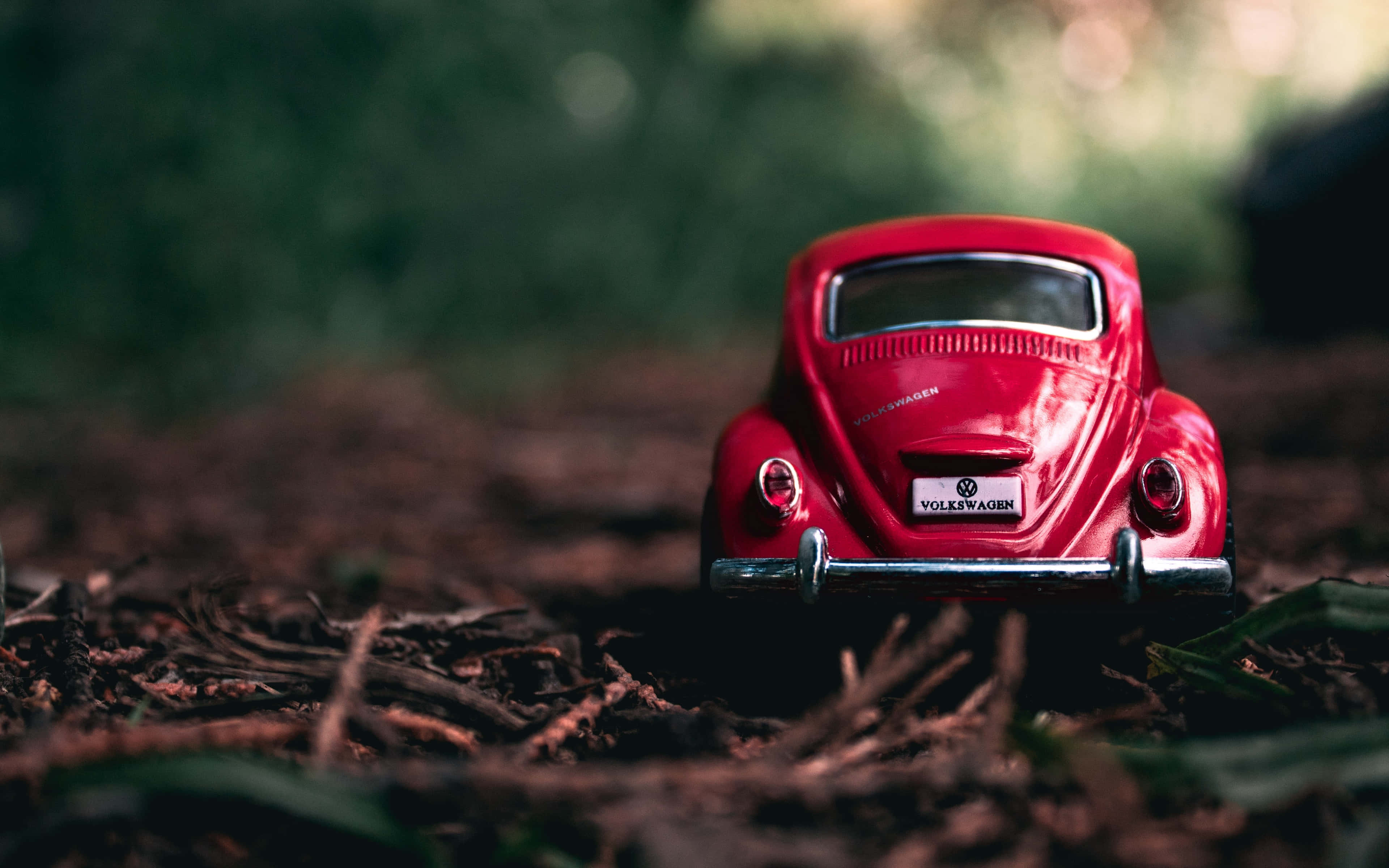 Vintage Car 桌布 壁紙 — 一輛光澤的紅色復古福斯金龜車玩具車放在森林地面覆蓋物上，背景是模糊的綠色樹葉。