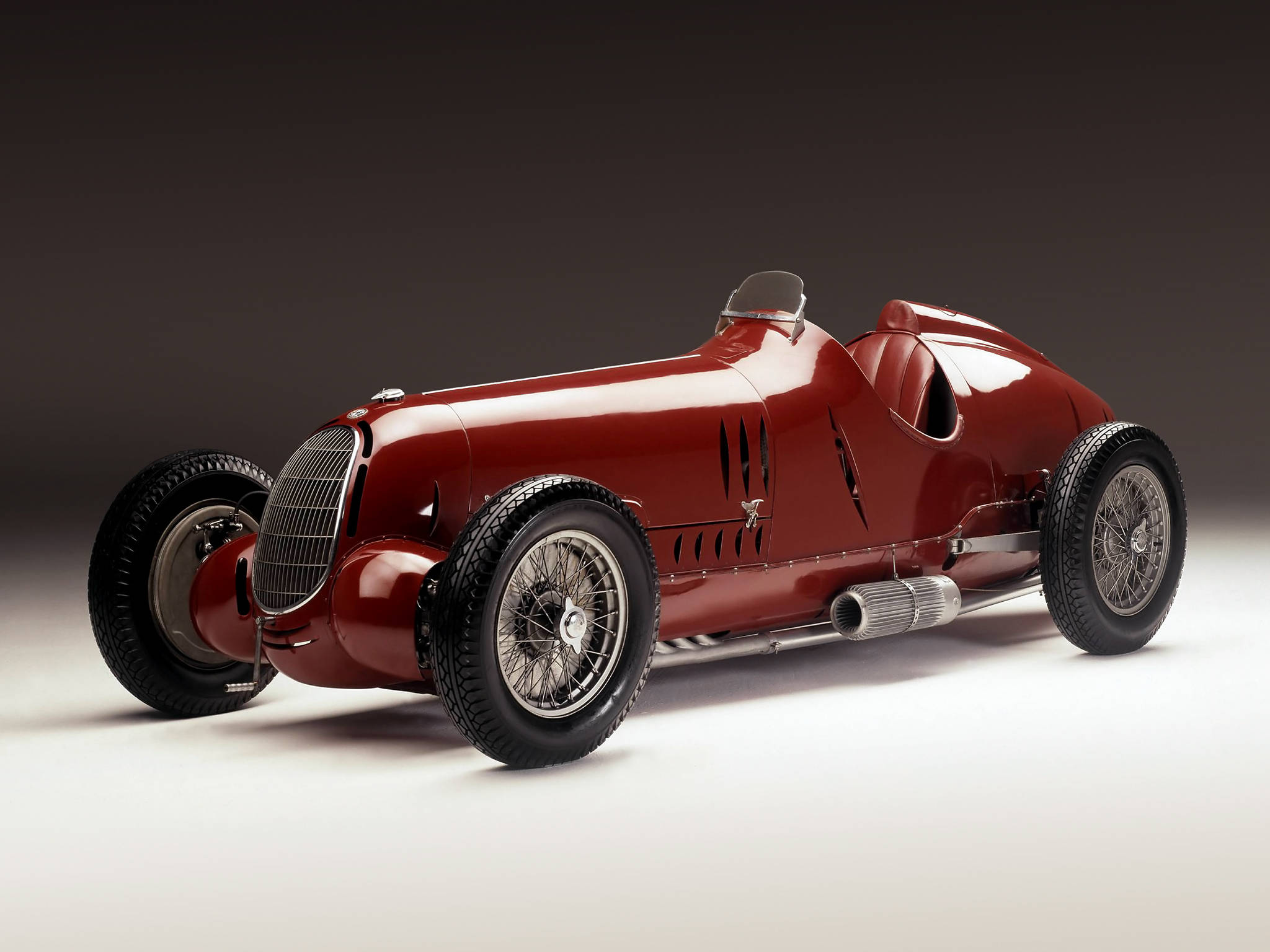 alfa romeo iPhone 桌布 壁紙 — 一輛光澤的紅色復古賽車，配有鋼絲輪轂和裸露的排氣管，在攝影棚燈光下閃閃發光。