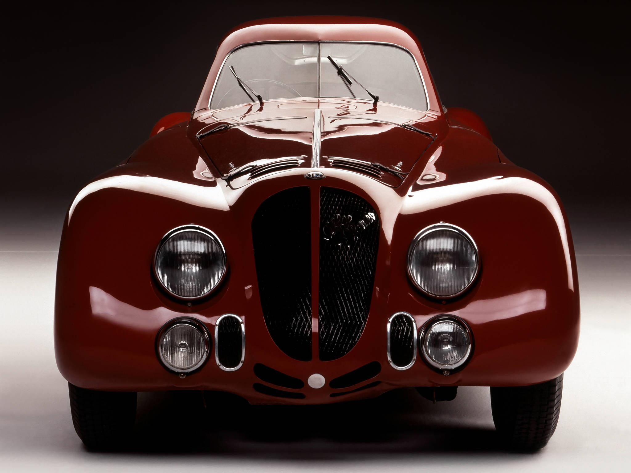 alfa romeo iPhone 桌布 壁紙 — 一輛光澤的紅色復古跑車，帶有鍍鉻裝飾和圓形頭燈，在攝影棚內以深色漸變背景拍攝。