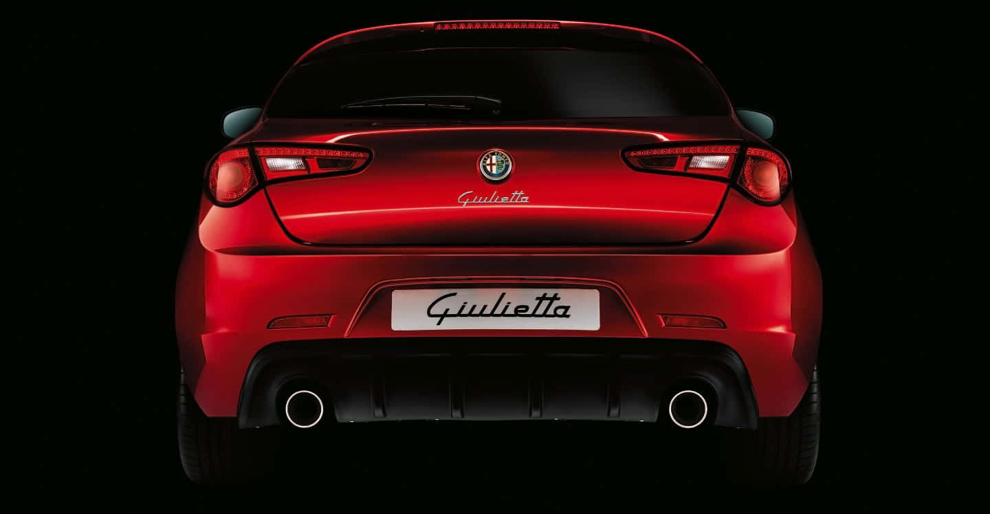 Alfa Romeo Giulietta 桌布 壁紙 — 一輛光澤的紅色愛快羅密歐 Giulietta 跑車，從後方觀看，背景為純黑色。