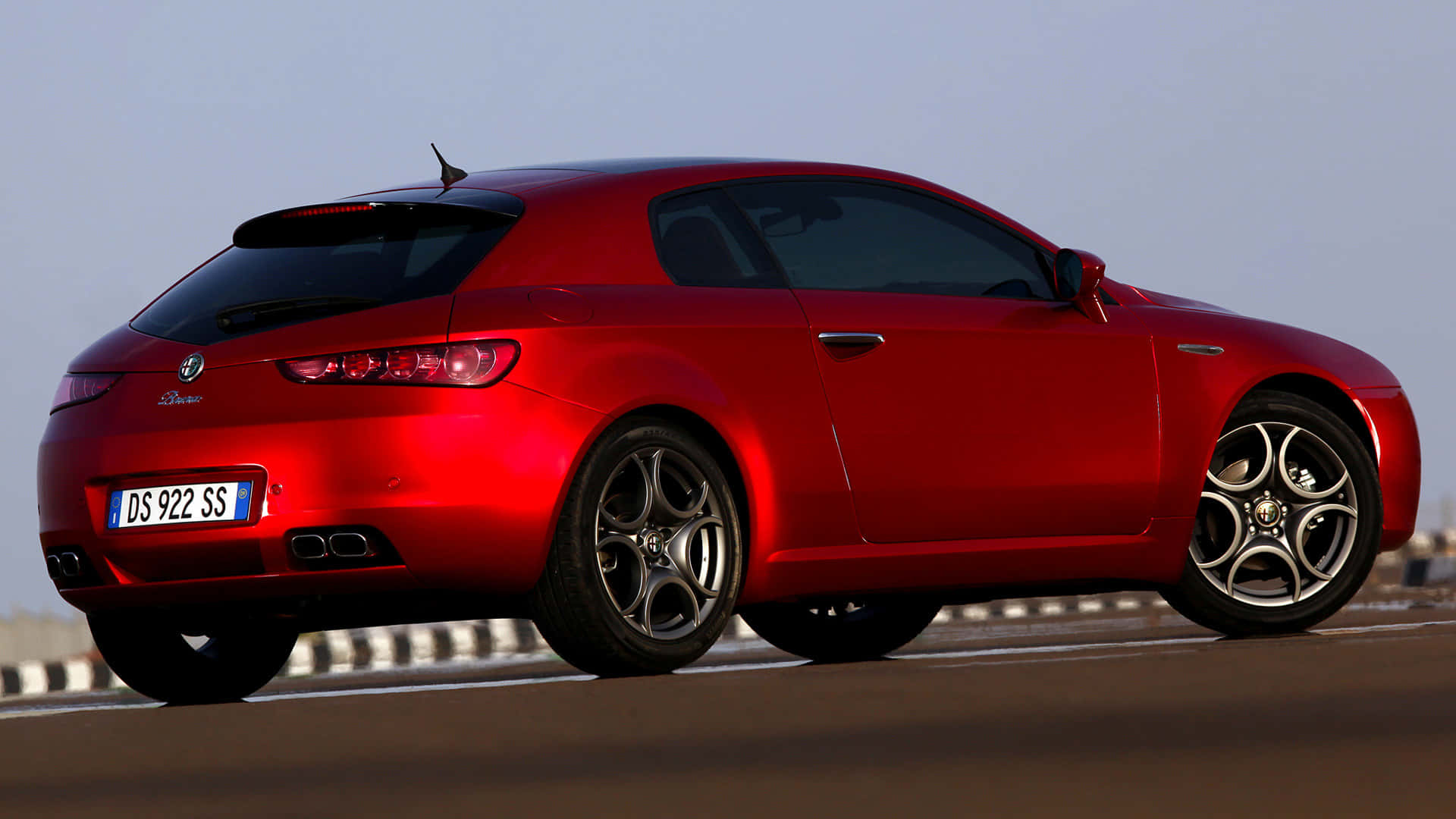 Alfa Romeo Brera 桌布 壁紙 — 一輛光澤的紅色愛快羅密歐Brera運動轎跑車，沿著陽光明媚的高速公路行駛，擁有流暢的曲線和合金輪圈。