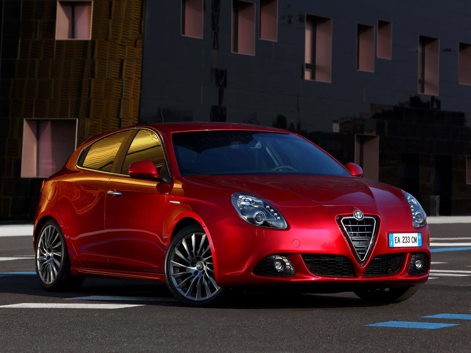Alfa Romeo Giulietta 桌布 壁紙 — 一輛光澤的紅色愛快羅密歐Giulietta停泊在城市的街道上，背景是現代建築。