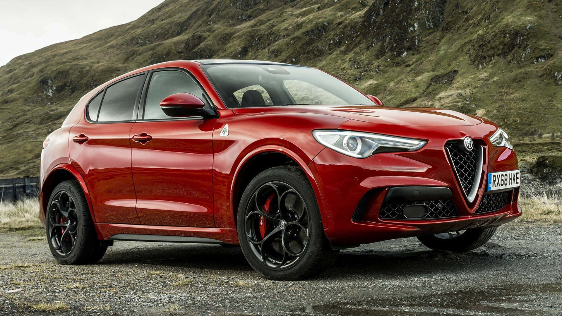 Alfa Romeo Stelvio 桌布 壁紙 — 一輛光澤的紅色愛快羅密歐Stelvio SUV停泊在碎石上，背景是長滿草的山丘。