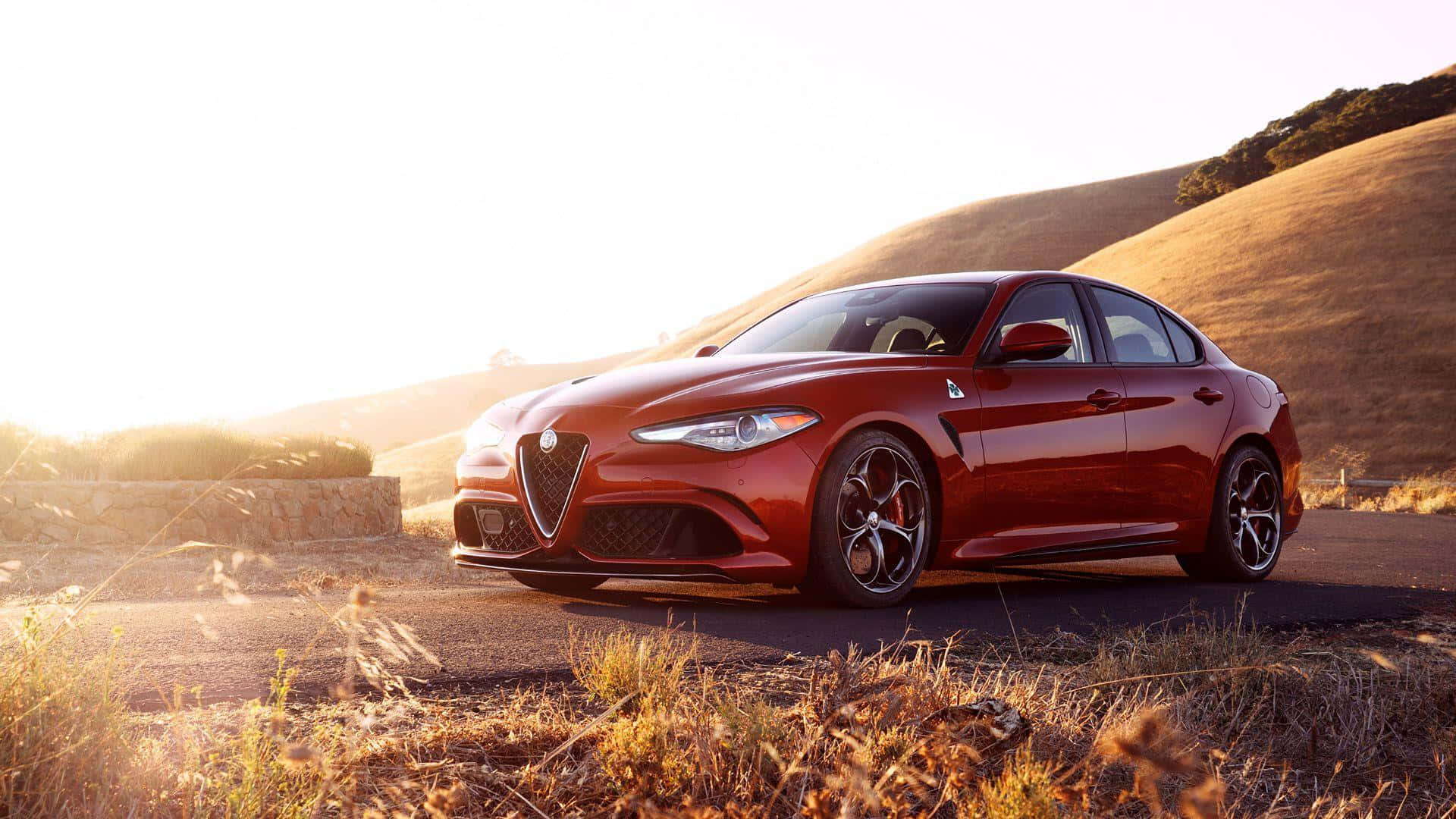 Alfa Romeo Giulia 桌布 壁紙 — 一輛光澤的紅色愛快羅密歐房車停泊在蜿蜒的道路上，正值黃金時刻，背景是起伏的山丘。