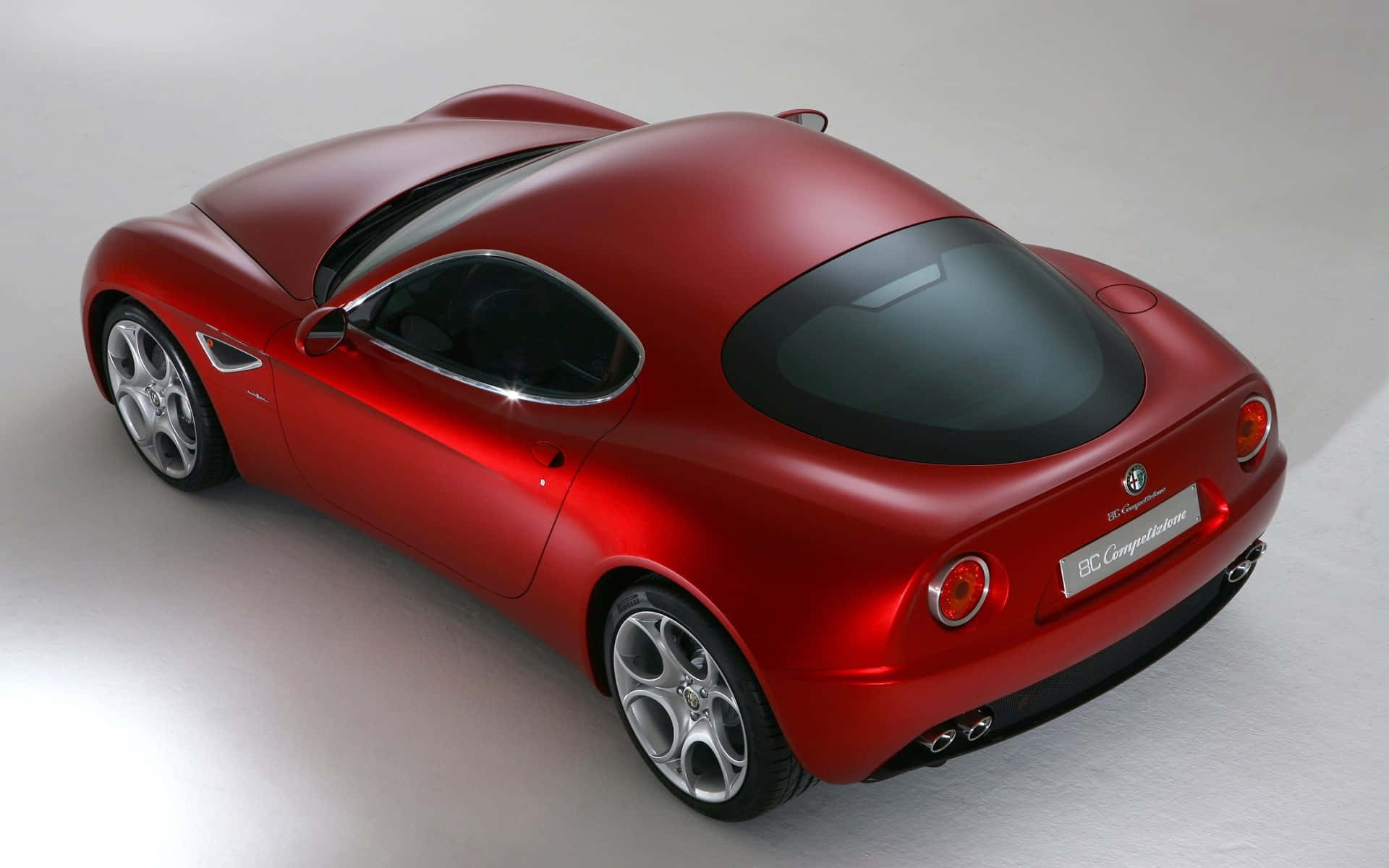 Alfa Romeo 8c Competizione 桌布 壁紙 — 一輛光澤的紅色愛快羅密歐跑車，擁有流線型曲線和銀色輪圈，從高後方角度在純白攝影棚背景前拍攝。