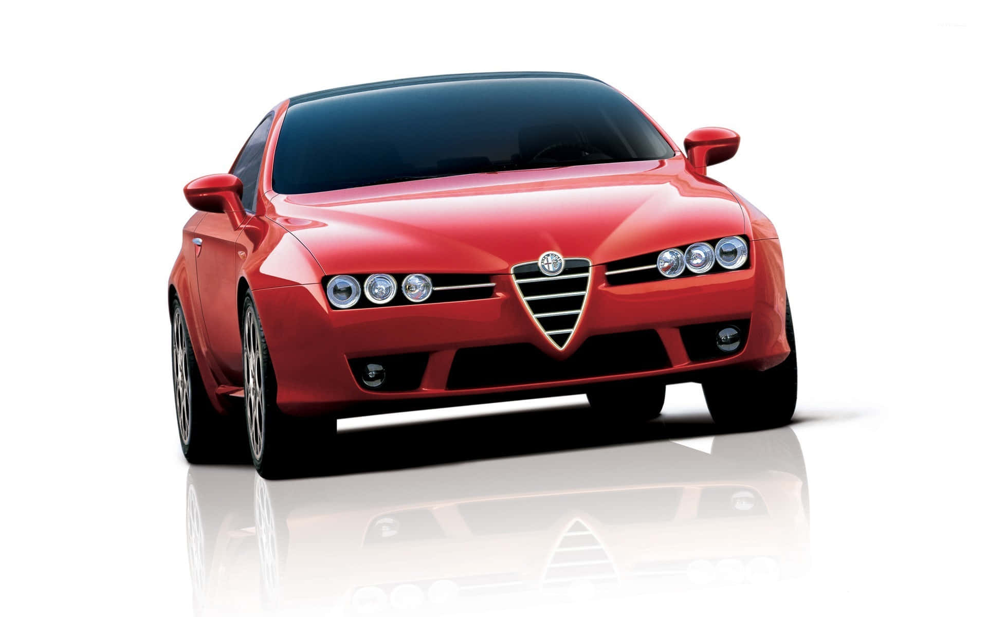 Alfa Romeo Brera 桌布 壁紙 — 一輛光澤的紅色愛快羅密歐跑車，配備四頭燈和標誌性水箱護罩，佇立在反光的白色攝影棚地板上。