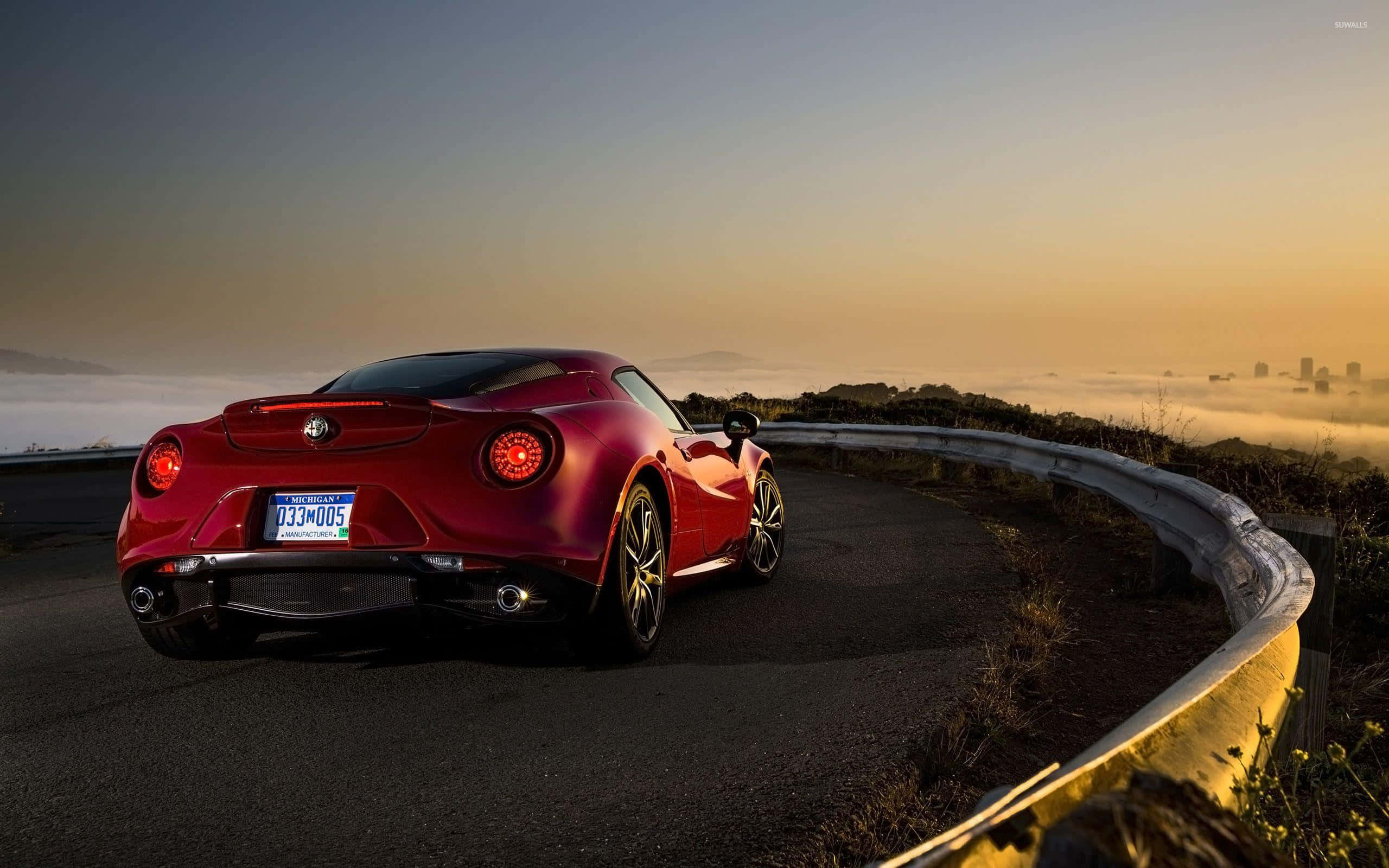 Alfa Romeo 4c 桌布 壁紙 — 一輛光澤的紅色愛快羅密歐跑車在日出時沿著蜿蜒的海岸道路行駛，下方有霧氣翻滾。