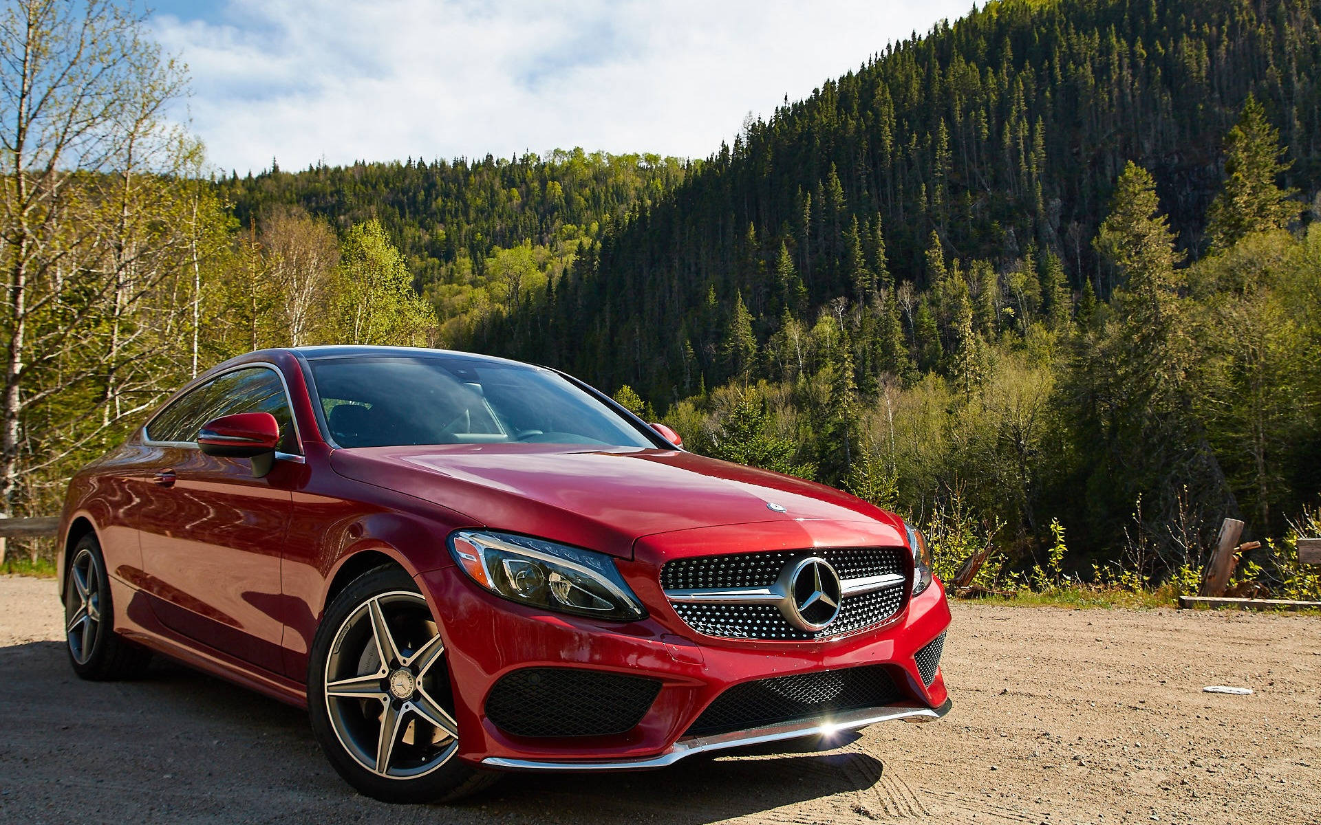 Mercedes Benz C300 桌布 壁紙 — 一輛光澤的紅色梅賽德斯C級轎跑車停在泥路上，背景是森林覆蓋的山脈，天空部分多雲。