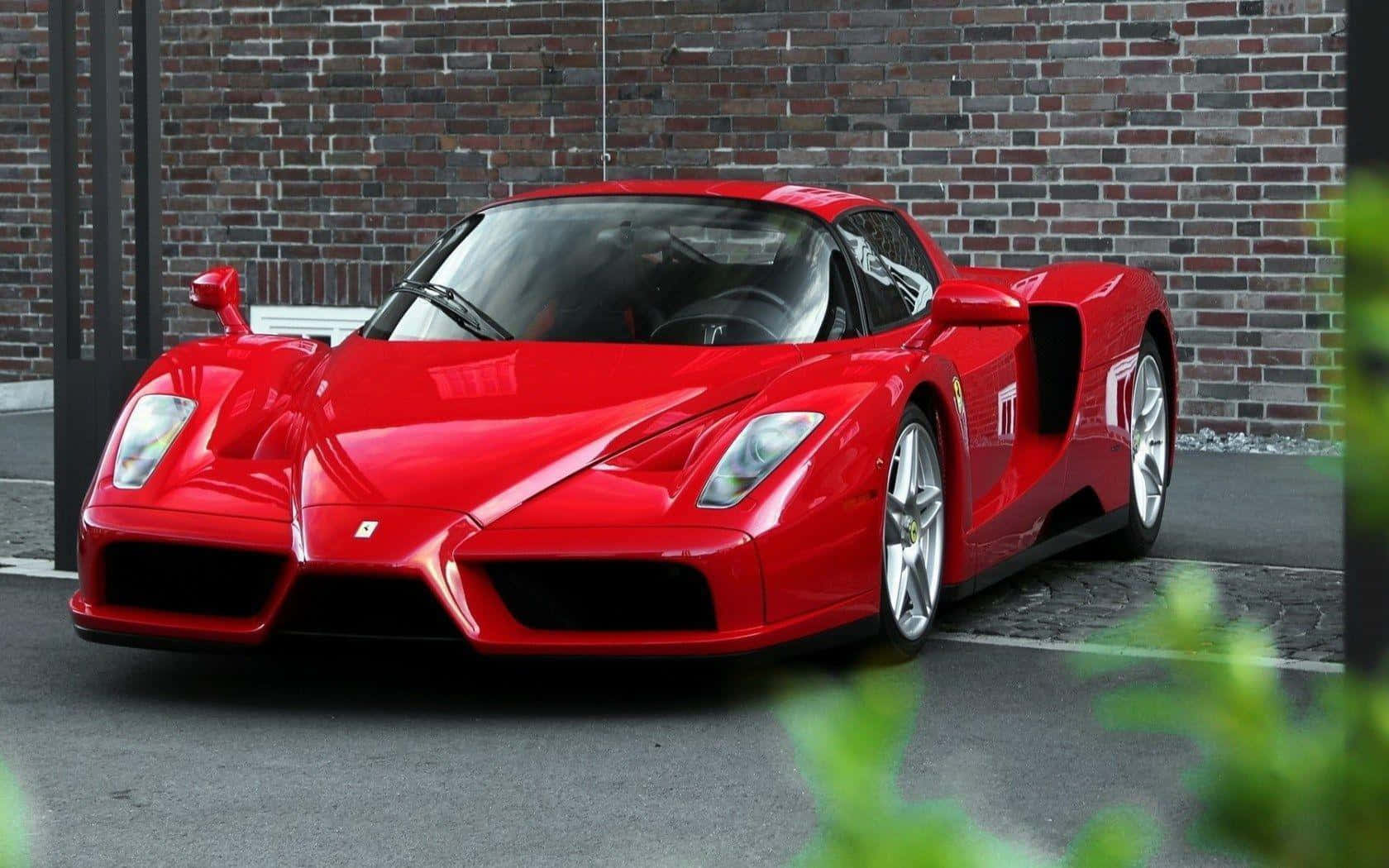Ferrari Enzo 桌布 壁紙 — 一輛光澤的紅色法拉利Enzo跑車停泊在風化的磚牆前，前景有綠色植物。
