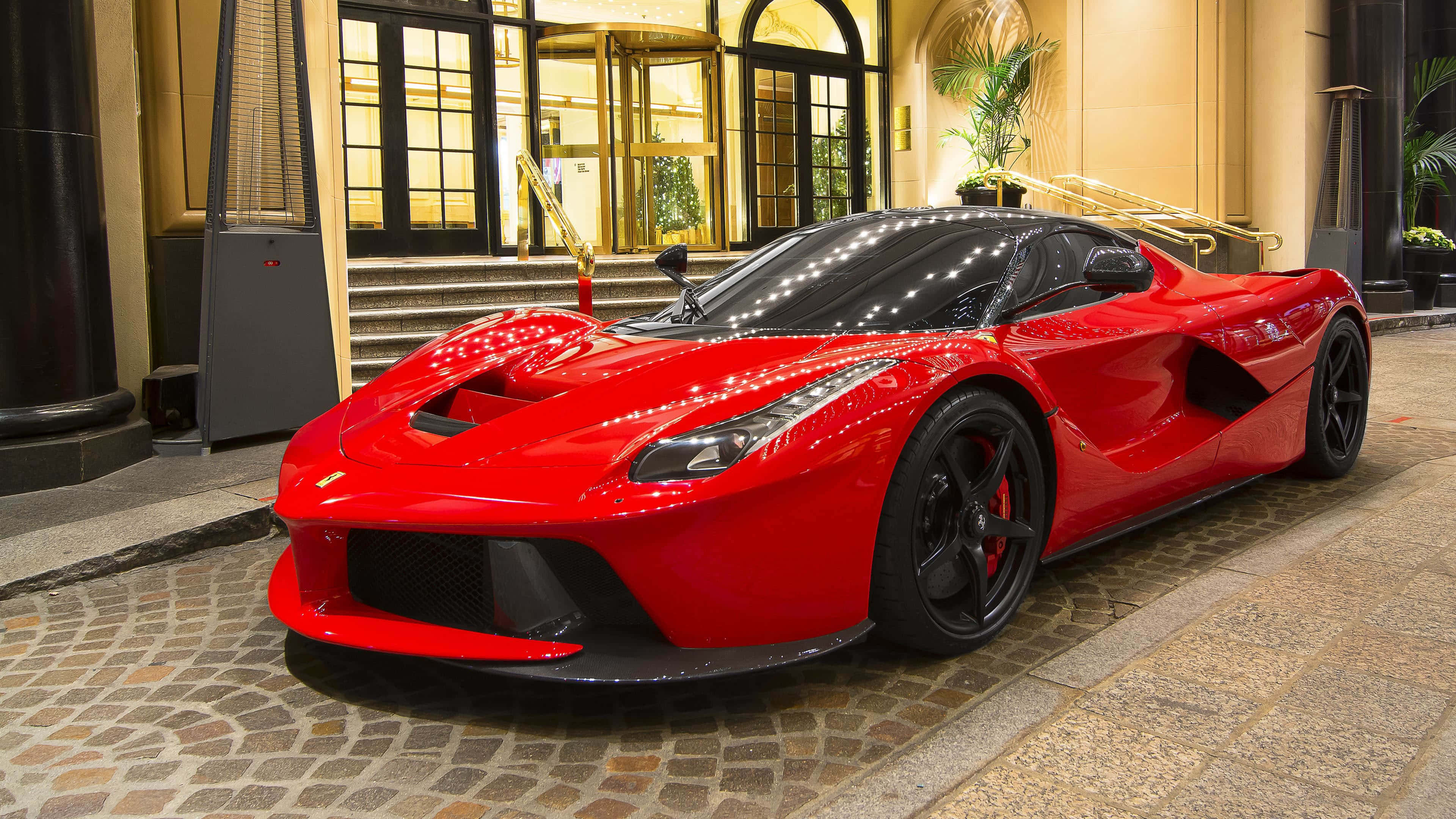 Ferrari Laferrari 桌布 壁紙 — 一輛光澤的紅色法拉利LaFerrari超級跑車在溫暖的燈光下閃耀，停在大飯店入口前的鵝卵石車道上。