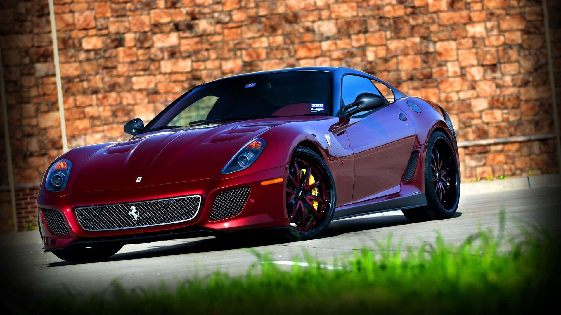 Ferrari 599 Gtb Fiorano 桌布 壁紙 — 一輛光澤的紅色法拉利跑車停放在風化的磚牆前，前景有充滿活力的綠色草地。