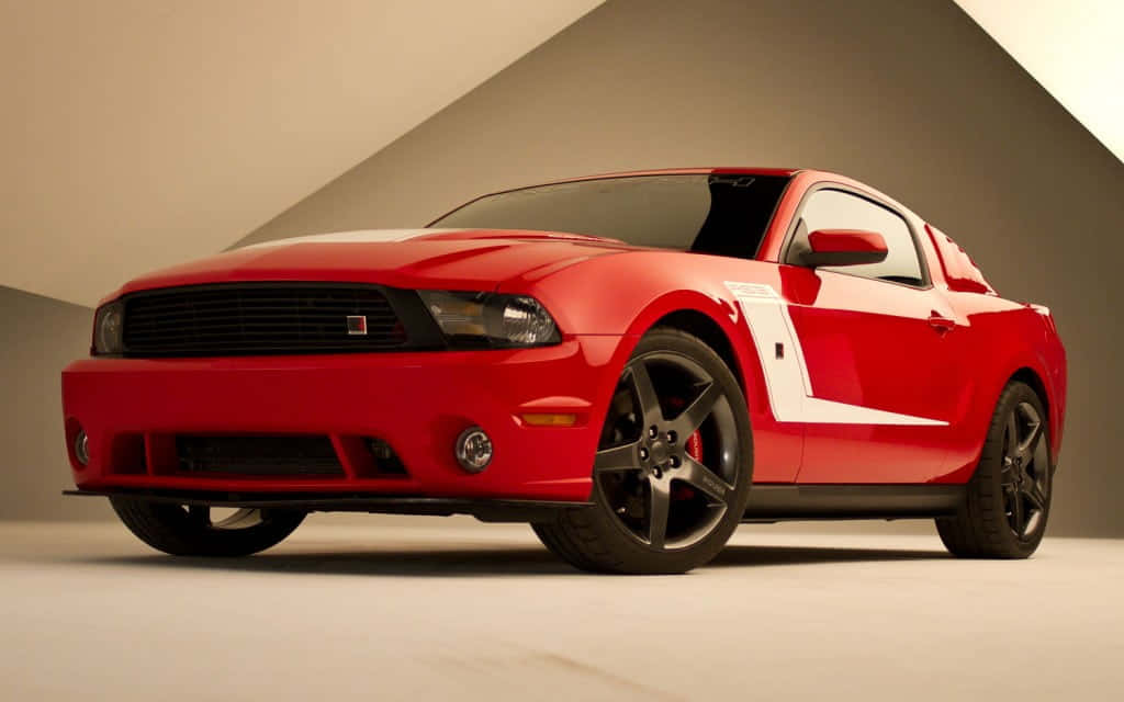 Ford Mustang Roush 桌布 壁紙 — 一輛光澤的紅色福特野馬Shelby GT500帶有白色賽車條紋，停在一個極簡主義的工作室中，背景是幾何米色牆壁。